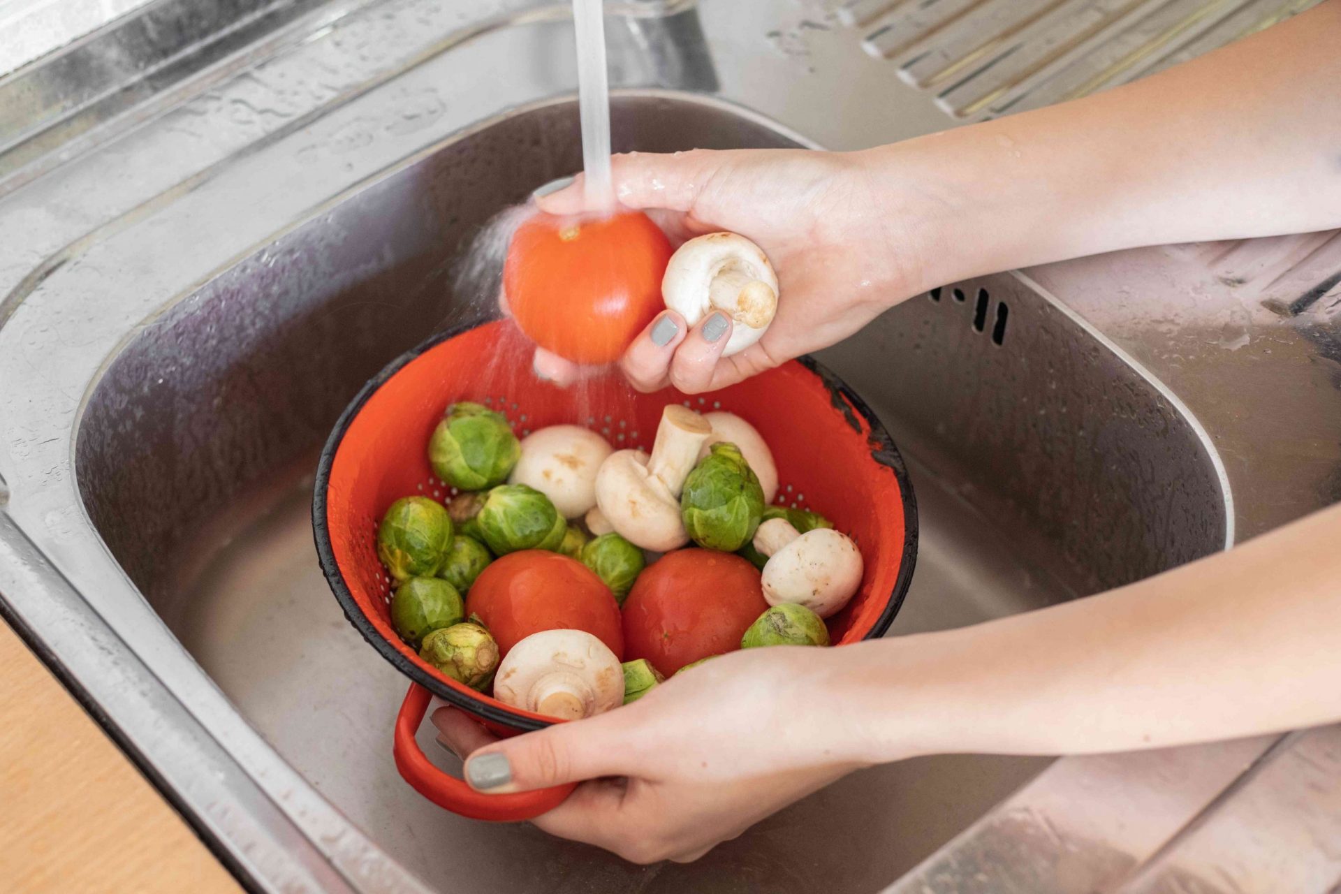 manos lavan un bol de verduras con agua en un fregadero de acero