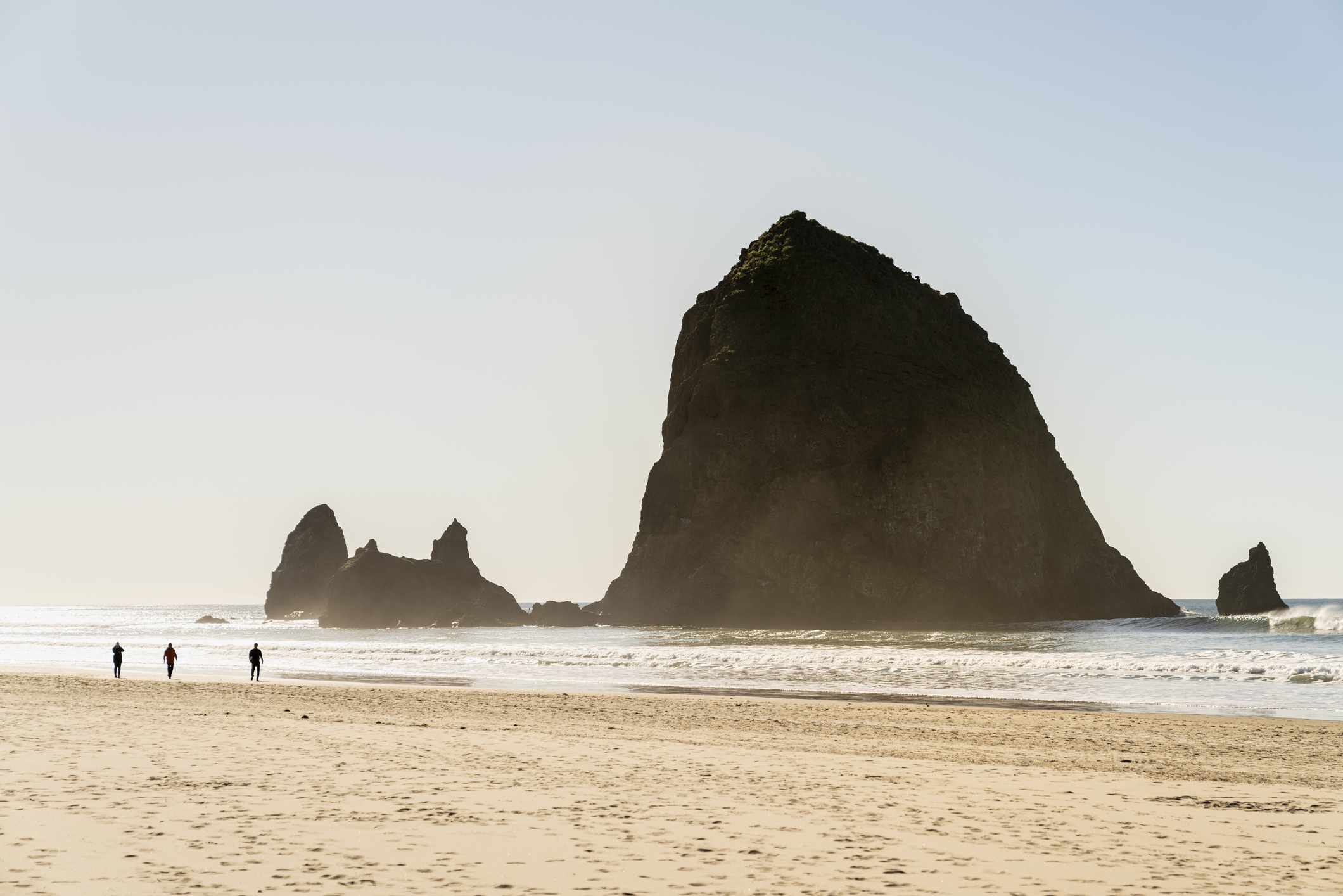 La gente camina por la playa frente a un gran monolito de roca en el océano