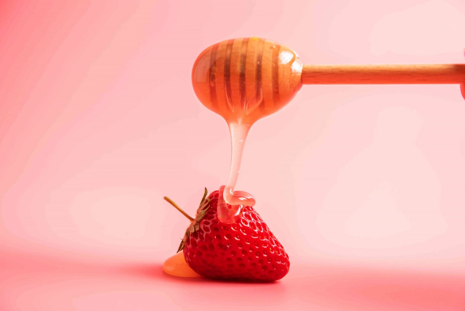 La miel gotea sobre la fresa sobre fondo rosa