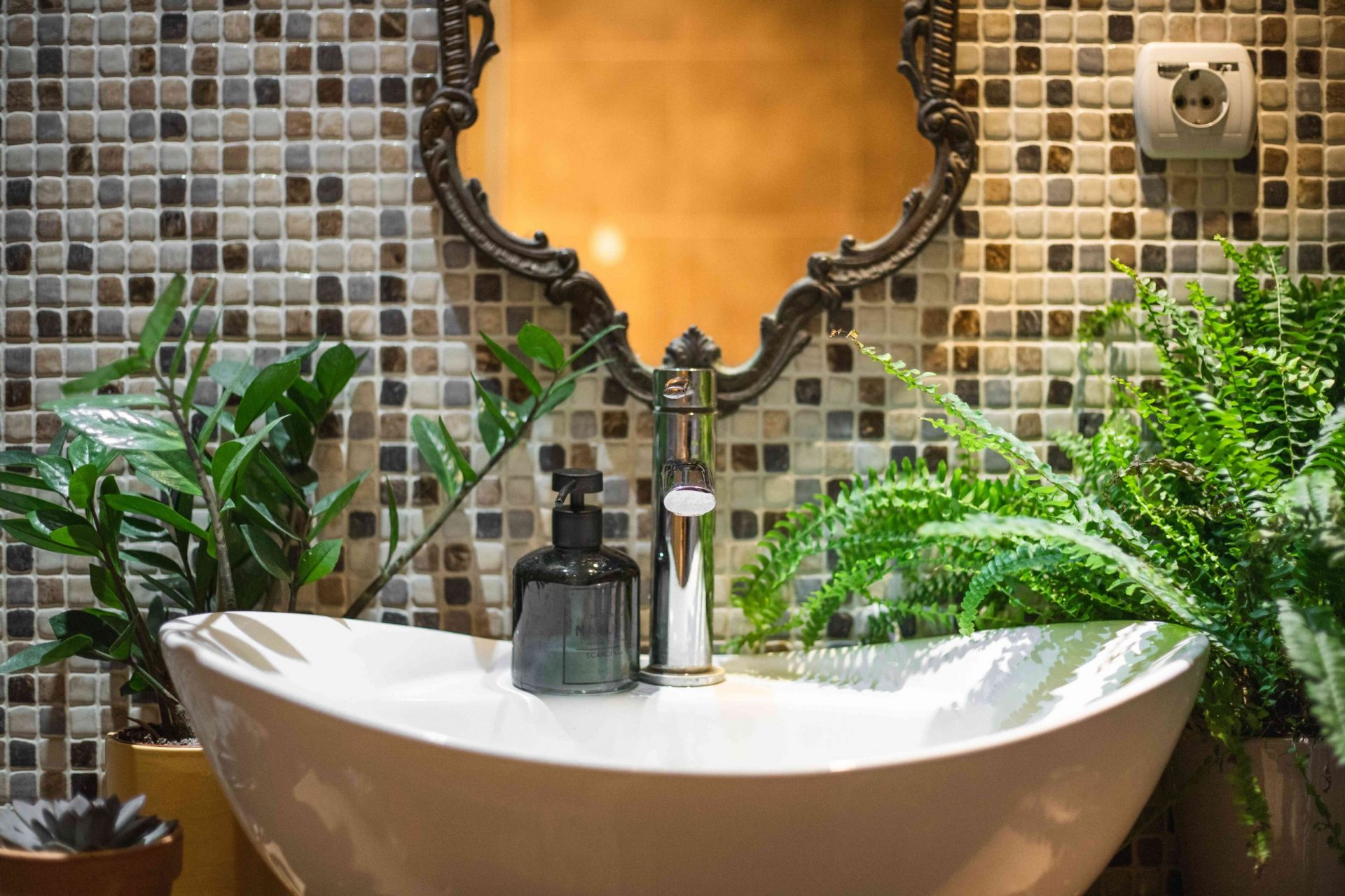 lavabo de baño grande con pared de azulejos rodeada de helechos y otras plantas de interior