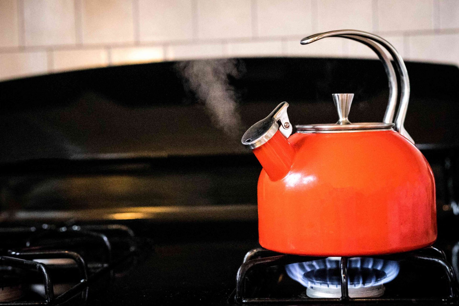 la tetera de color rojo tomate echa vapor en la cocina de gas