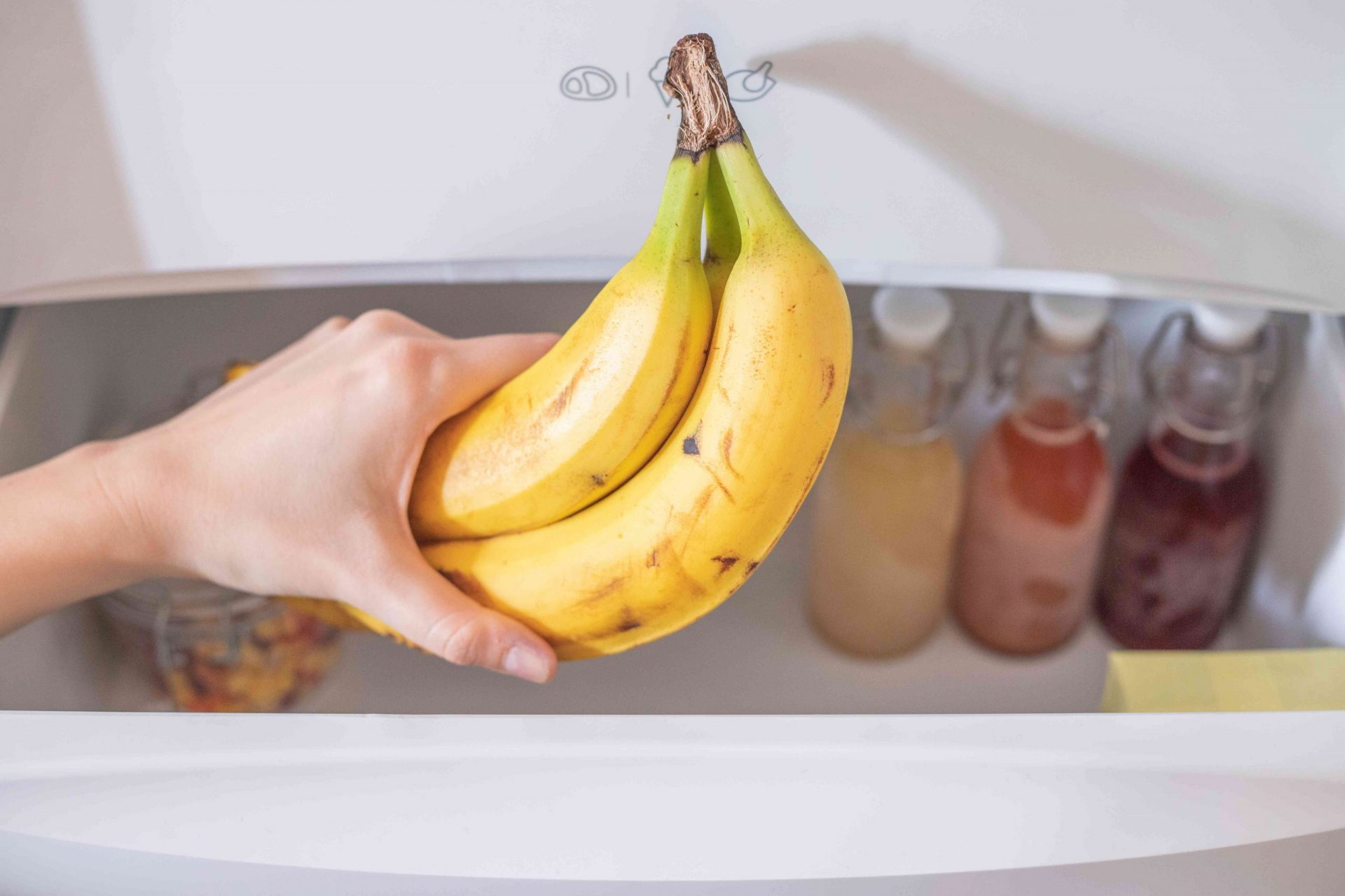 manos sostienen un racimo de plátanos sobre el cajón abierto del congelador con otros alimentos congelados
