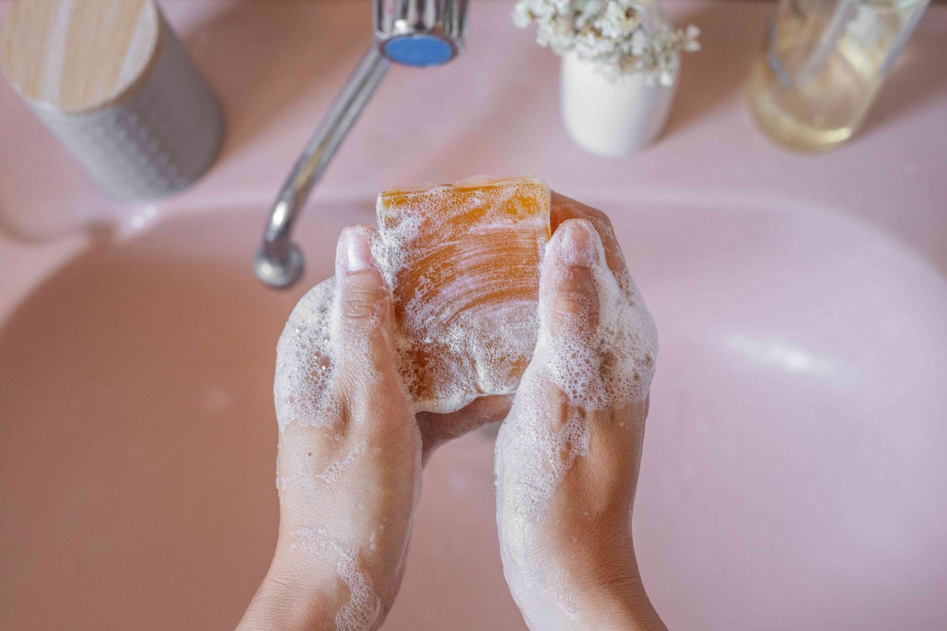 una mujer se lava las manos con jabón natural en un lavabo rosa