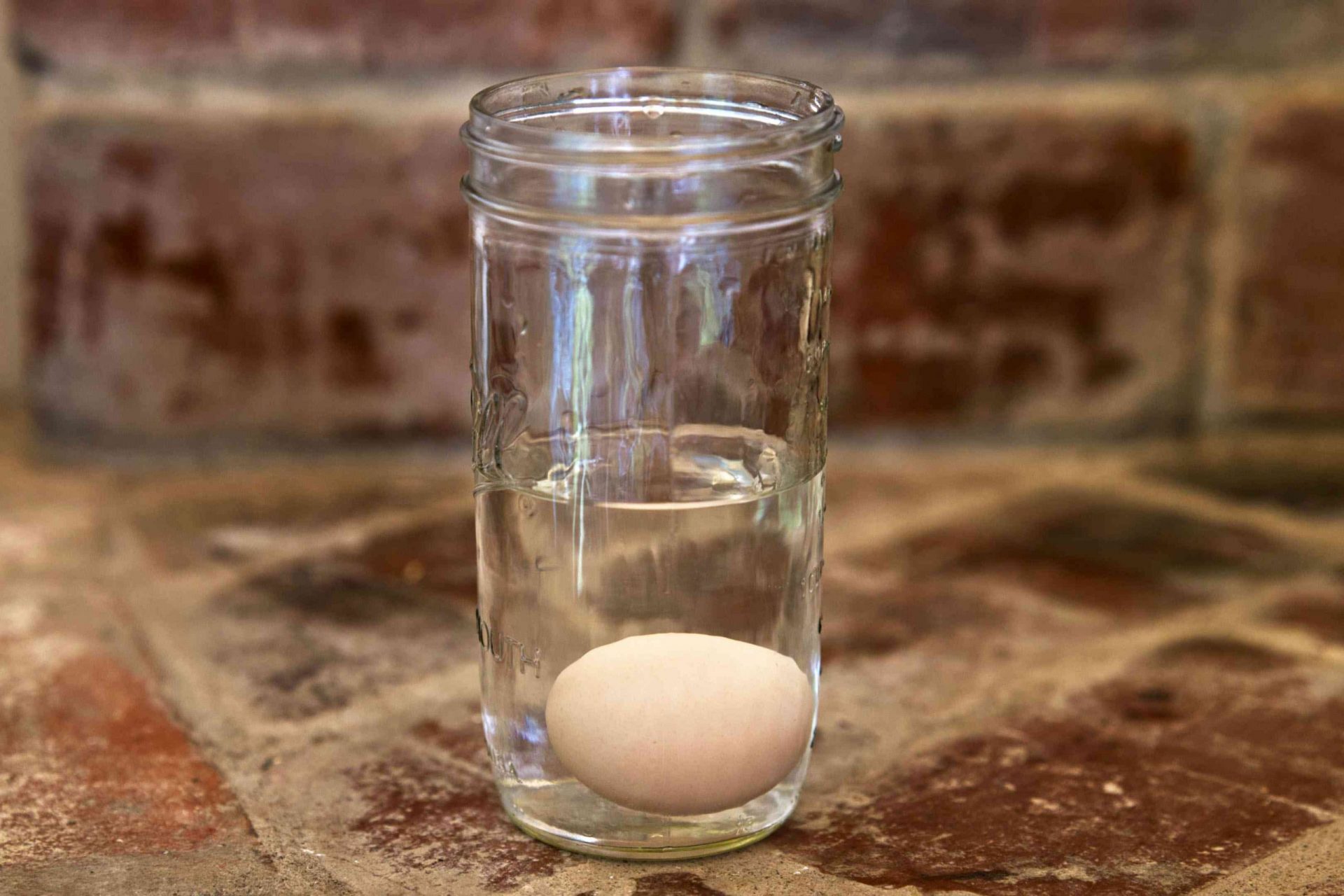 prueba de flotación del huevo en un tarro de cristal lleno de agua sobre la encimera de piedra
