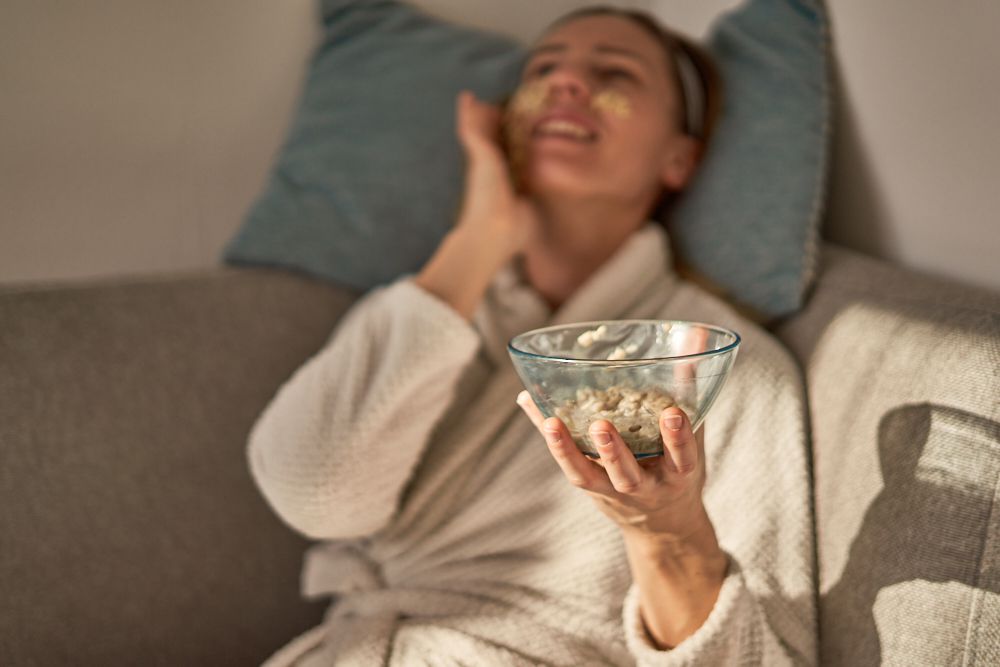 mujer reclinada sobre una almohada mientras sostiene un cuenco de cristal lleno de una mascarilla facial de avena DIY