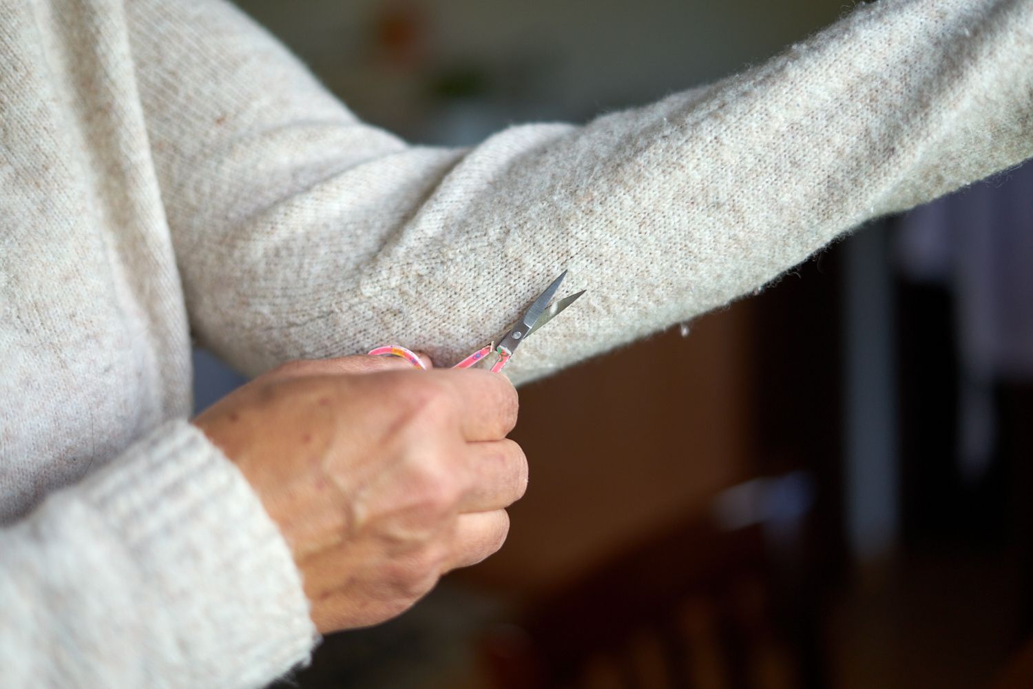 persona con jersey de color crema corta cuidadosamente las pastillas del brazo extendido con unas tijeras pequeñas