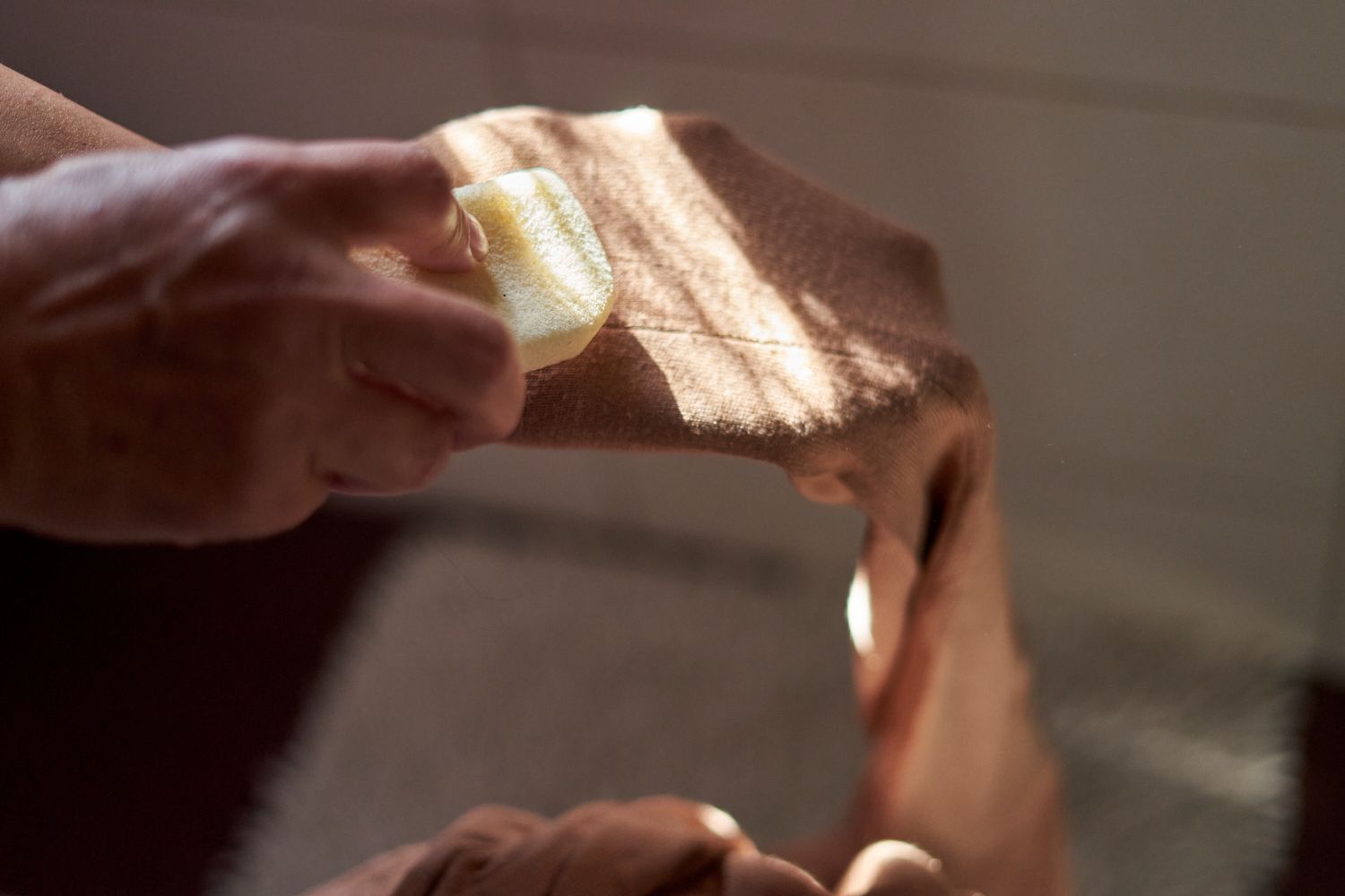 manos frotan suavemente una piedra pómez de color crema en el brazo del jersey marrón para eliminar las pastillas