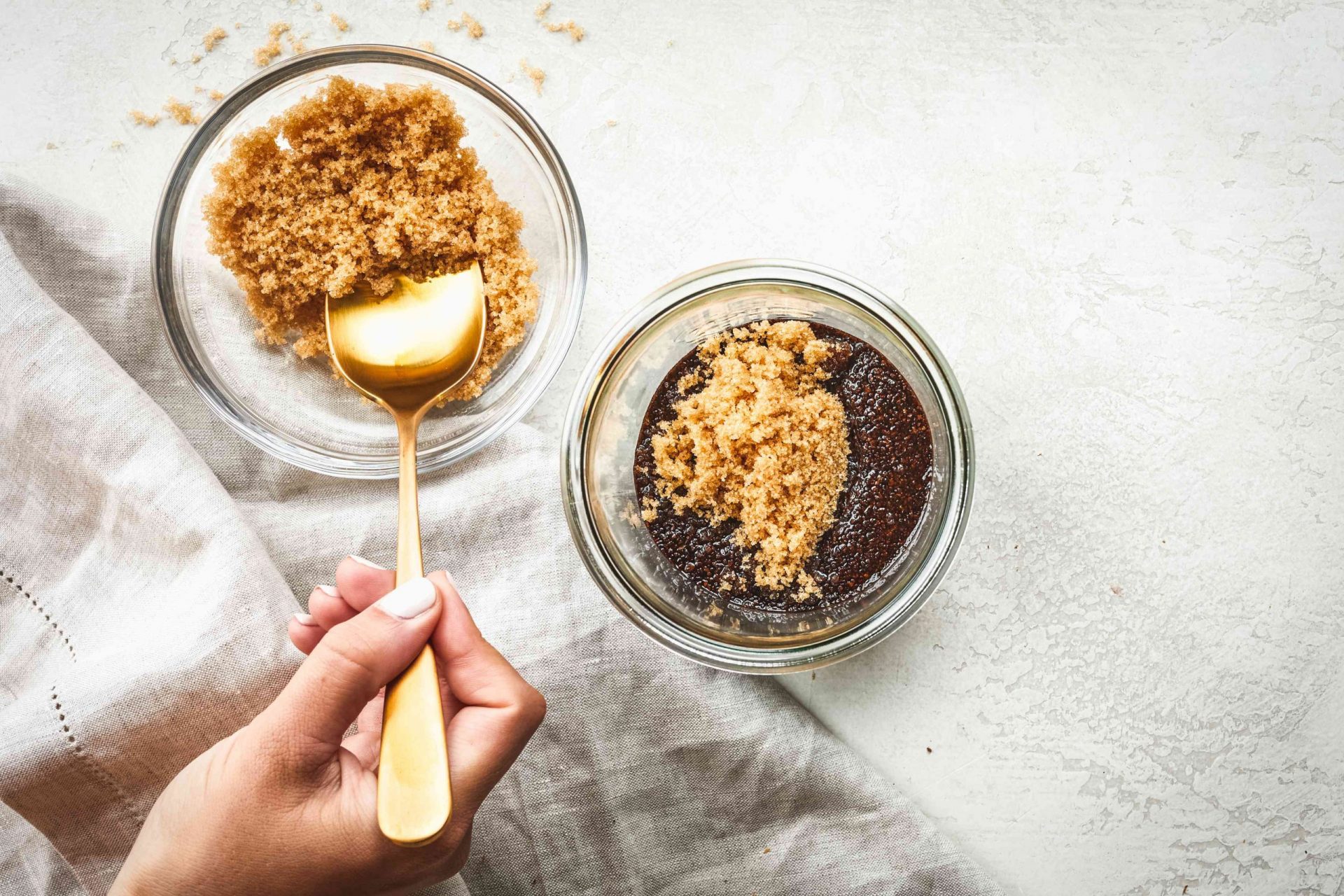 La cuchara dorada saca el azúcar moreno del bol de cristal y lo añade a la mezcla de café y aceite de coco
