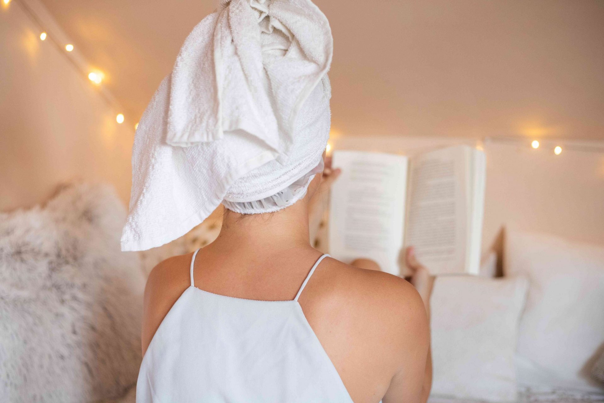 espalda de mujer con gorro de ducha y toalla envuelta mientras lee un libro