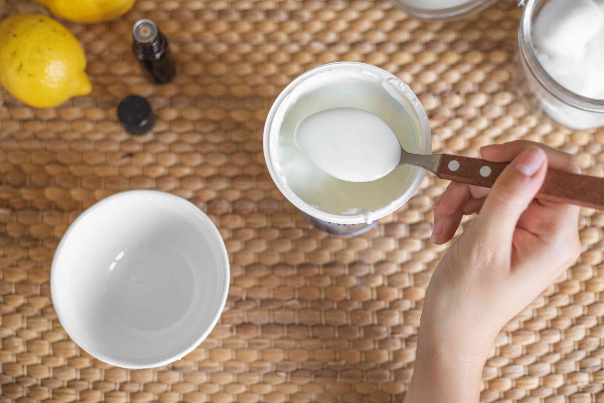 la mano mide las cucharadas de yogur de la taza en el bol de cerámica blanco