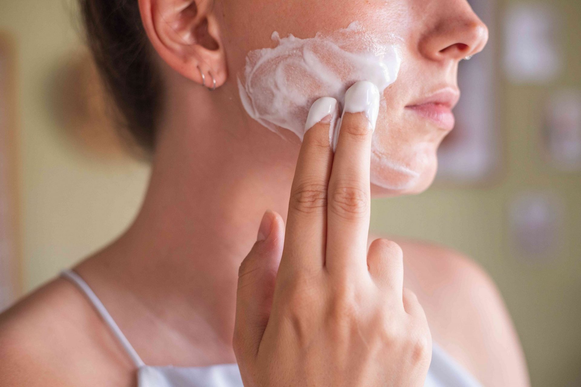 perfil lateral de una mujer aplicando una mascarilla casera de yogur en la mejilla con dos dedos