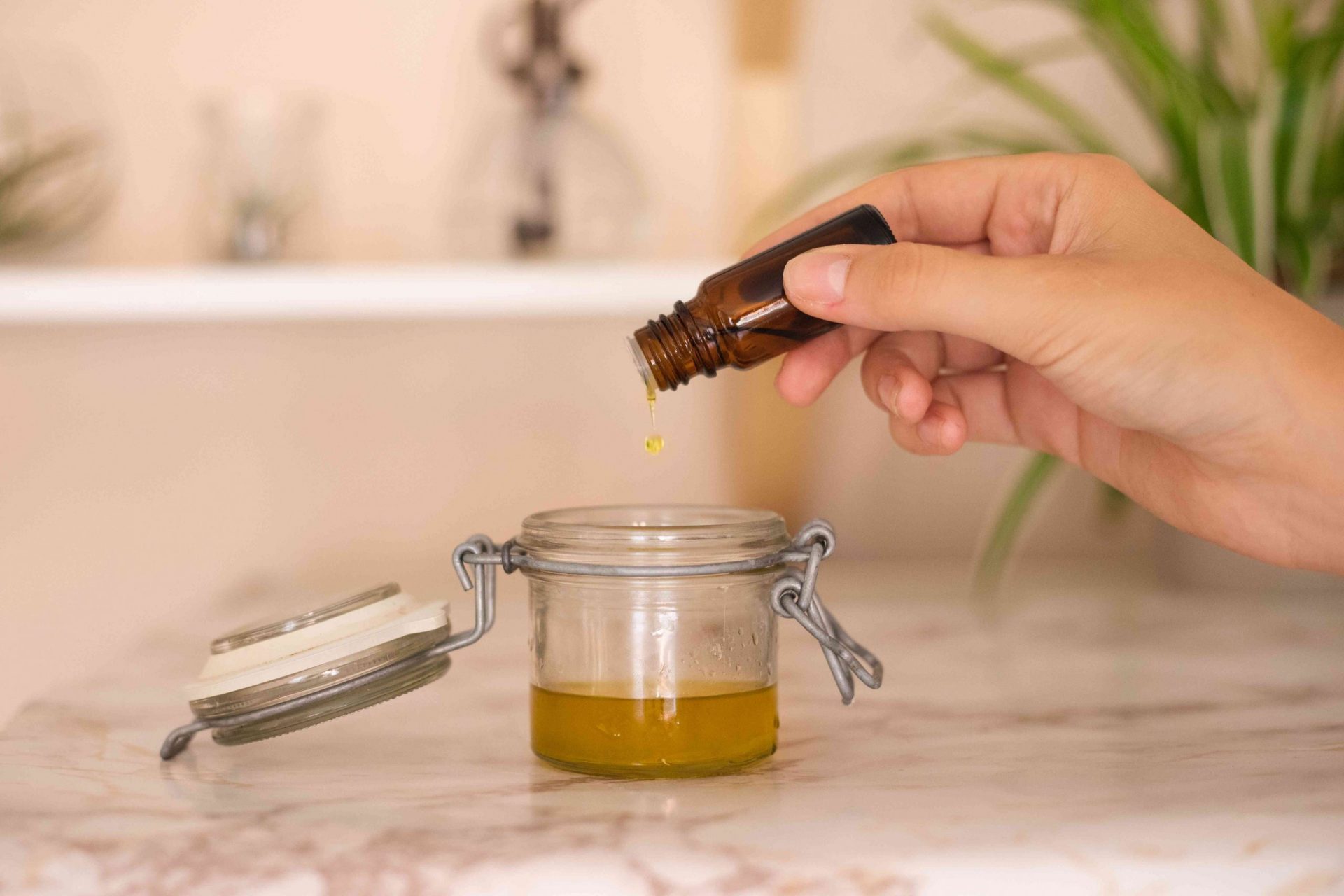 la mano añade una gota de aceite esencial al recipiente de cristal del aceite de oliva calentado