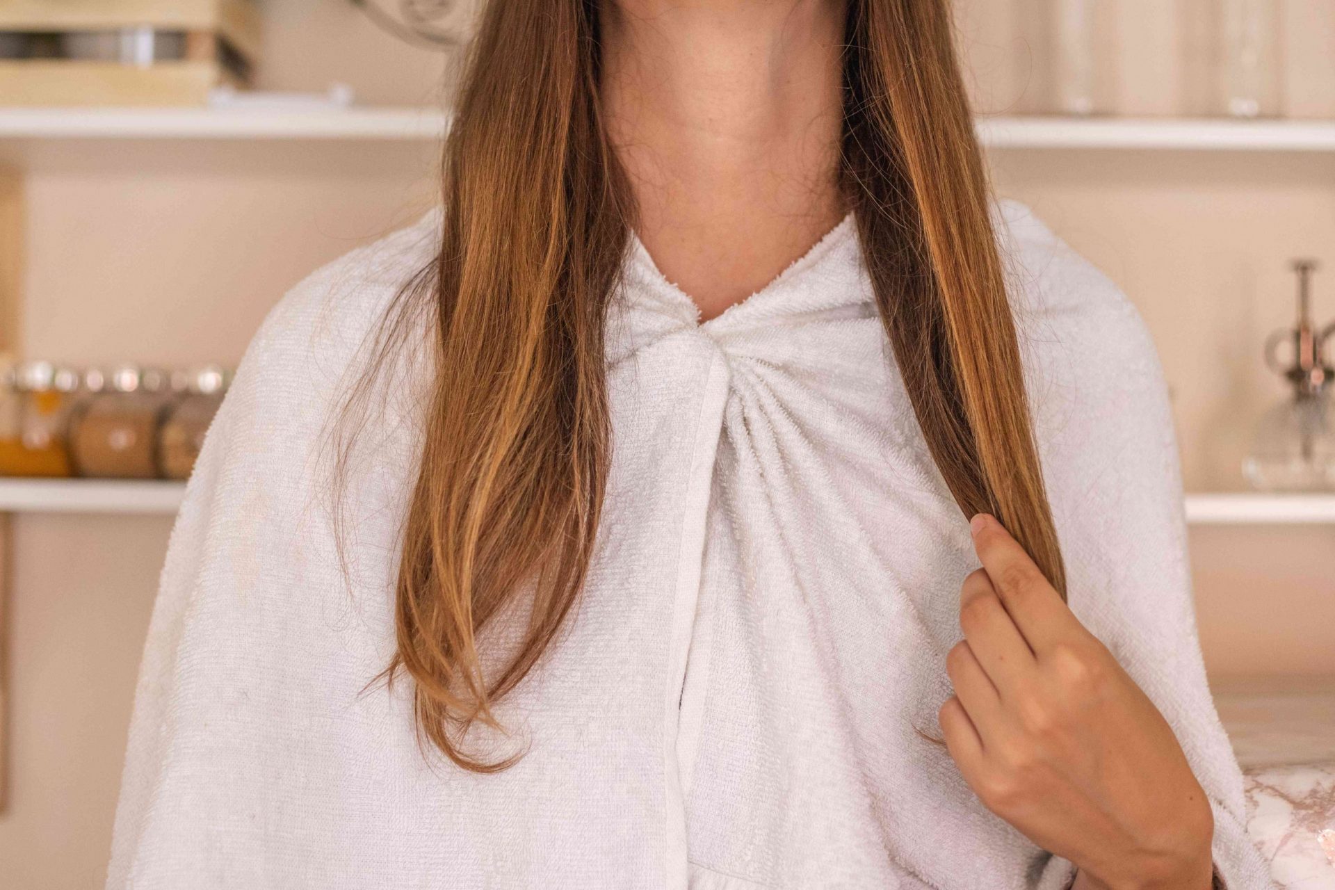mujer con una toalla alrededor de los hombros aplica la mascarilla de aceite de oliva en las puntas del pelo largo