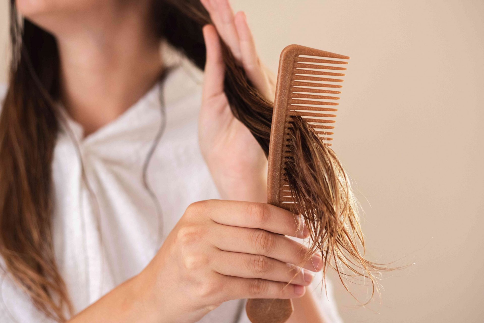 una mujer utiliza un peine marrón para desenredar su largo cabello castaño