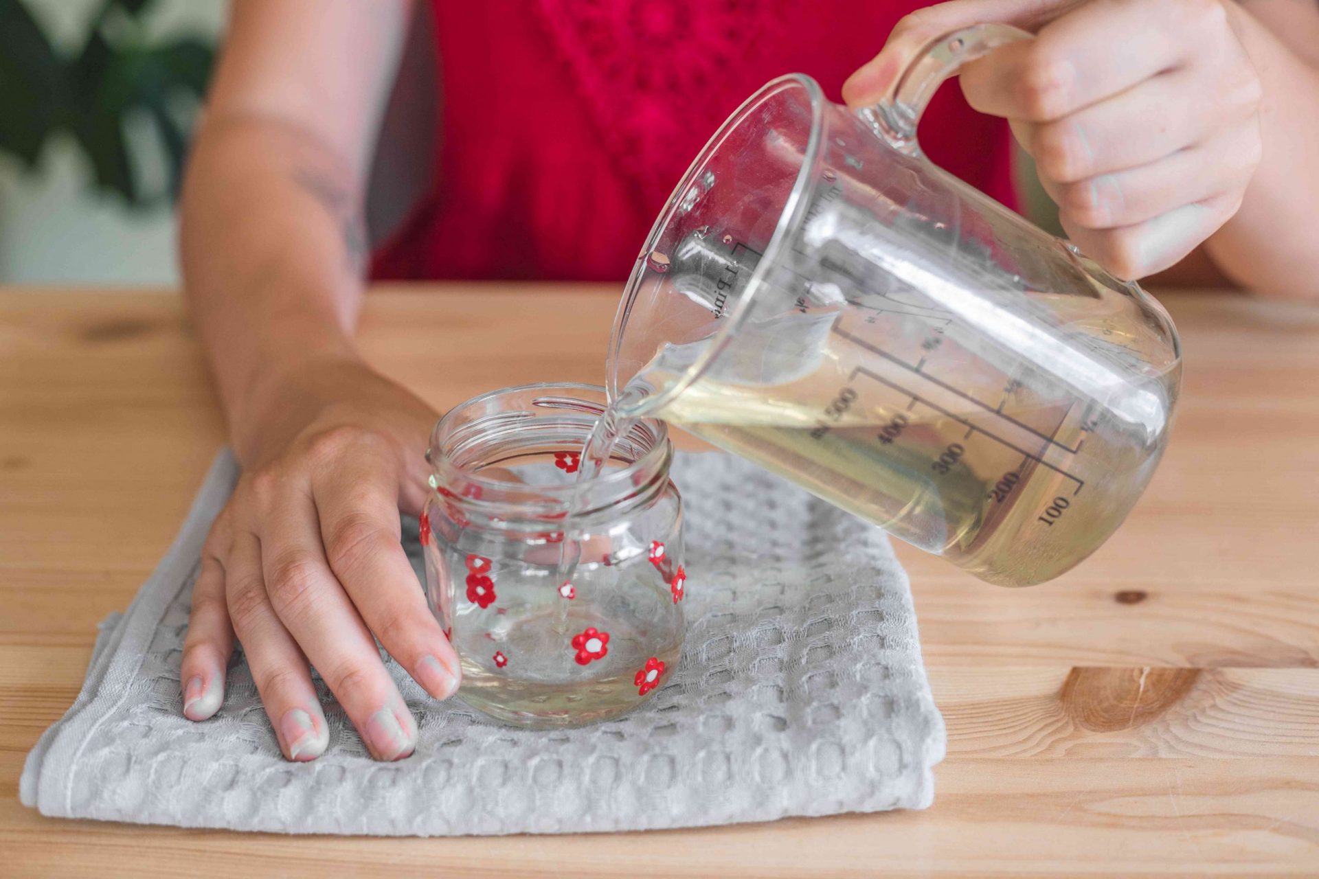 mujer con camisa roja vierte la mezcla de azúcar y agua en un alimentador de colibríes de cristal