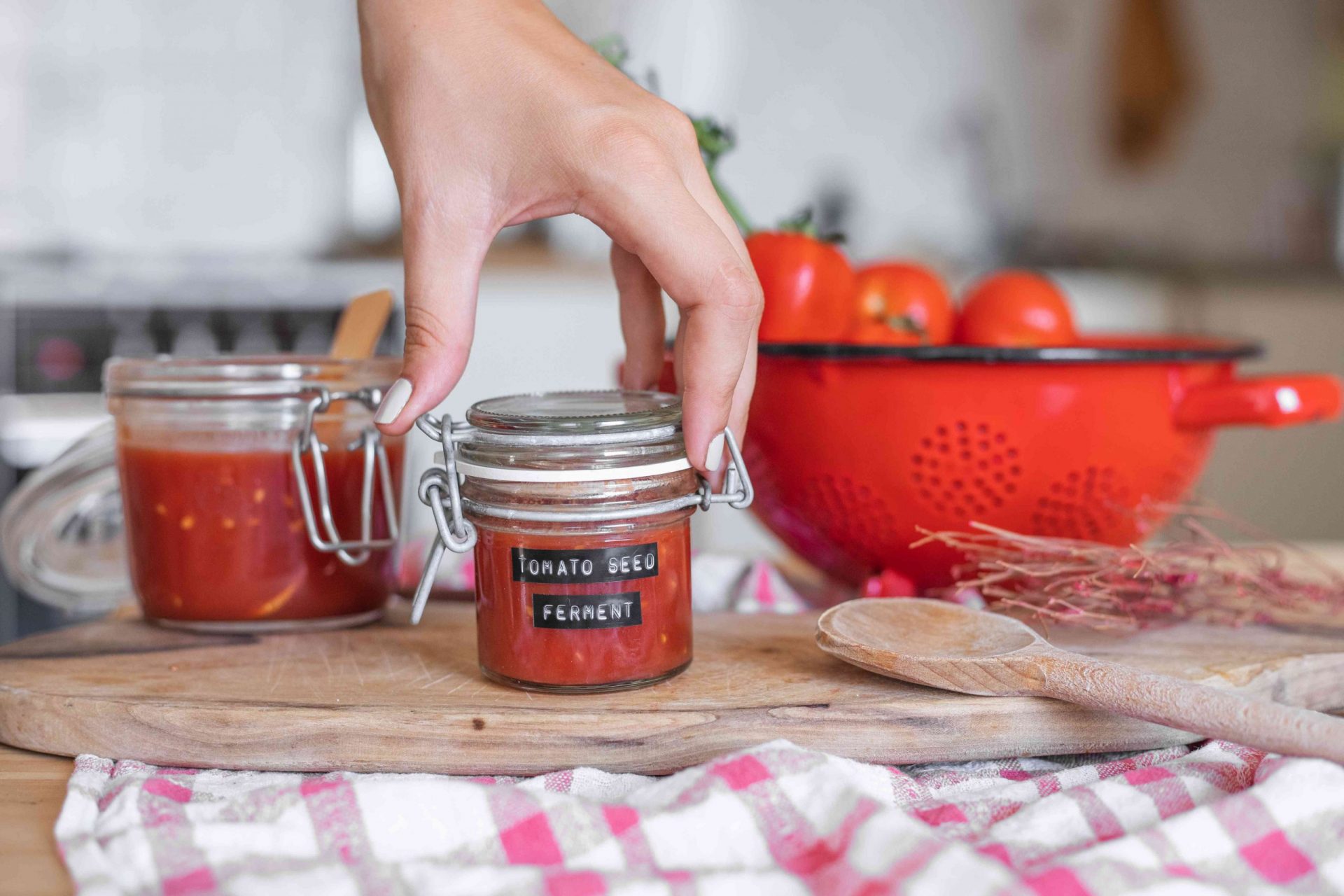 las manos alcanzan el tarro de cristal con tapa etiquetado como fermentación de semillas de tomate en la mesa de la cocina