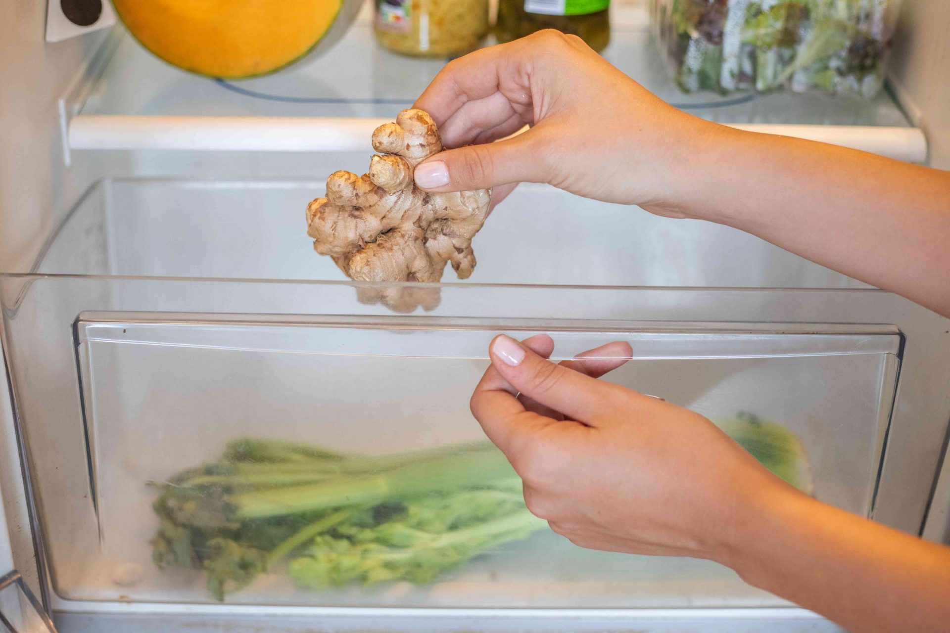 una mujer coloca un ajo fresco sin pelar en el cajón del frigorífico junto al apio
