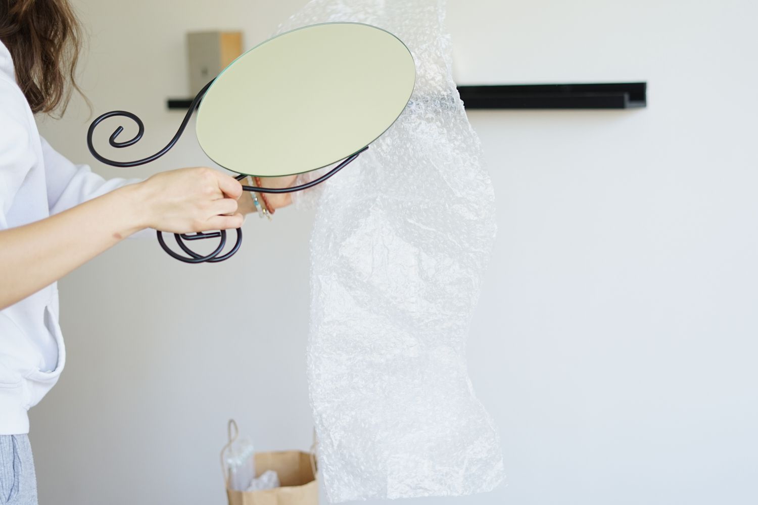 una persona de pie envuelve con plástico de burbujas un frágil espejo de cristal sobre un soporte