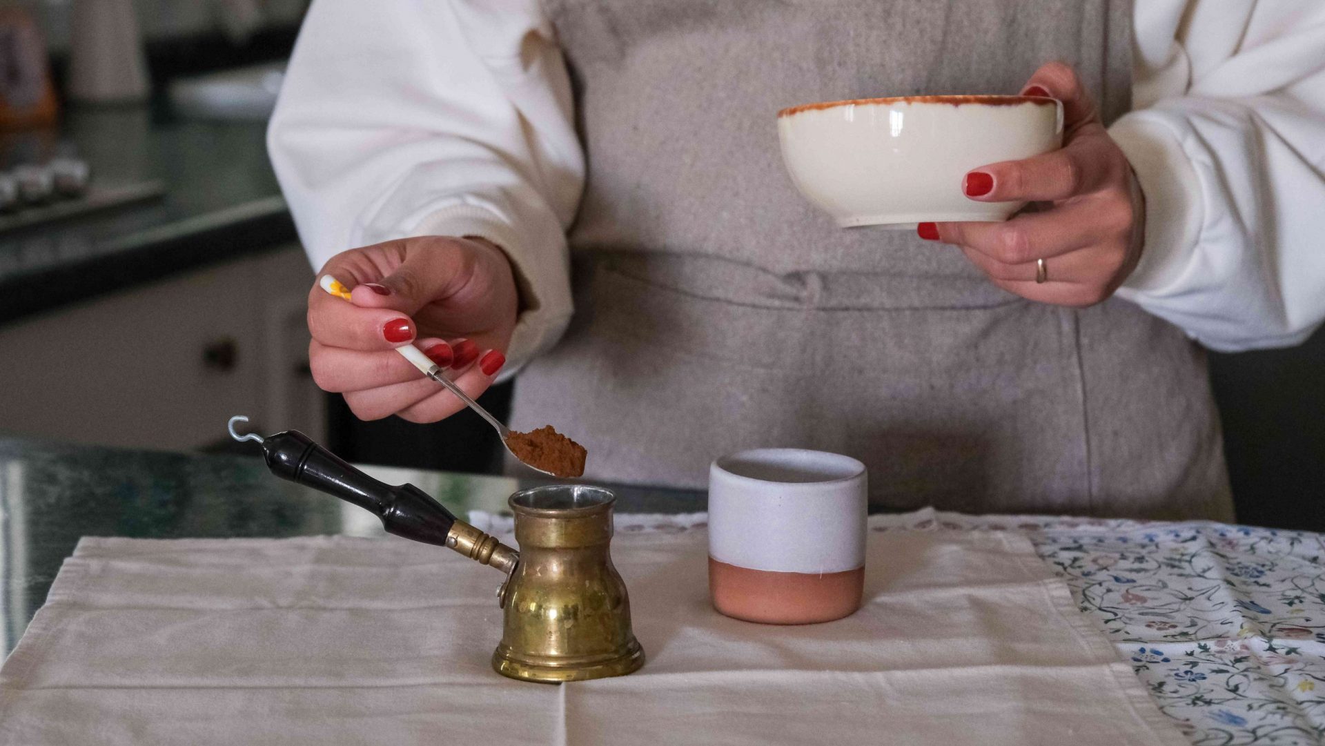 foto de cintura de una persona preparando café turco con una taza de cerámica y una cafetera turca de latón