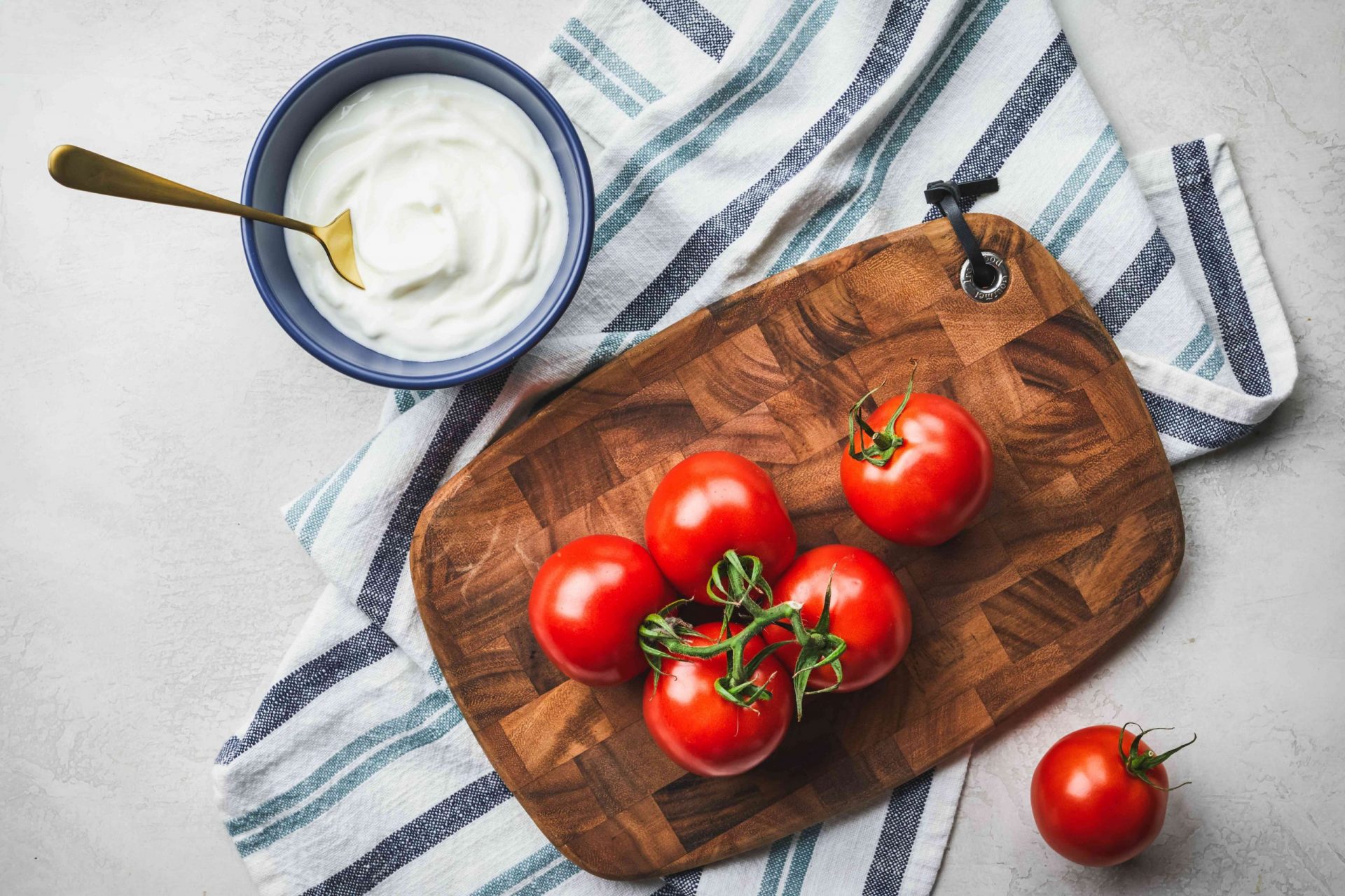 posición plana de tomates en rama sobre una tabla de cortar de madera junto a un bol de yogur griego