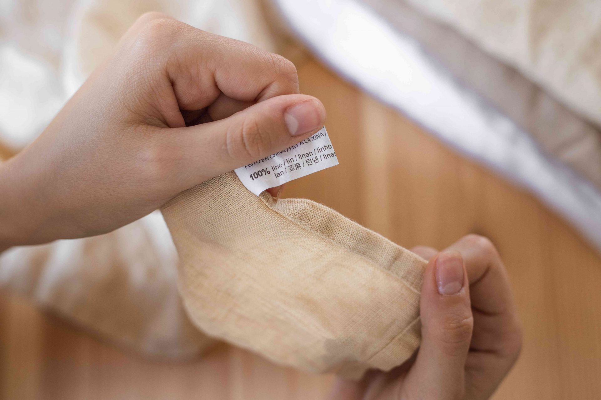 unas manos sostienen una tela de lino de color tostado mostrando la etiqueta de 100% lino