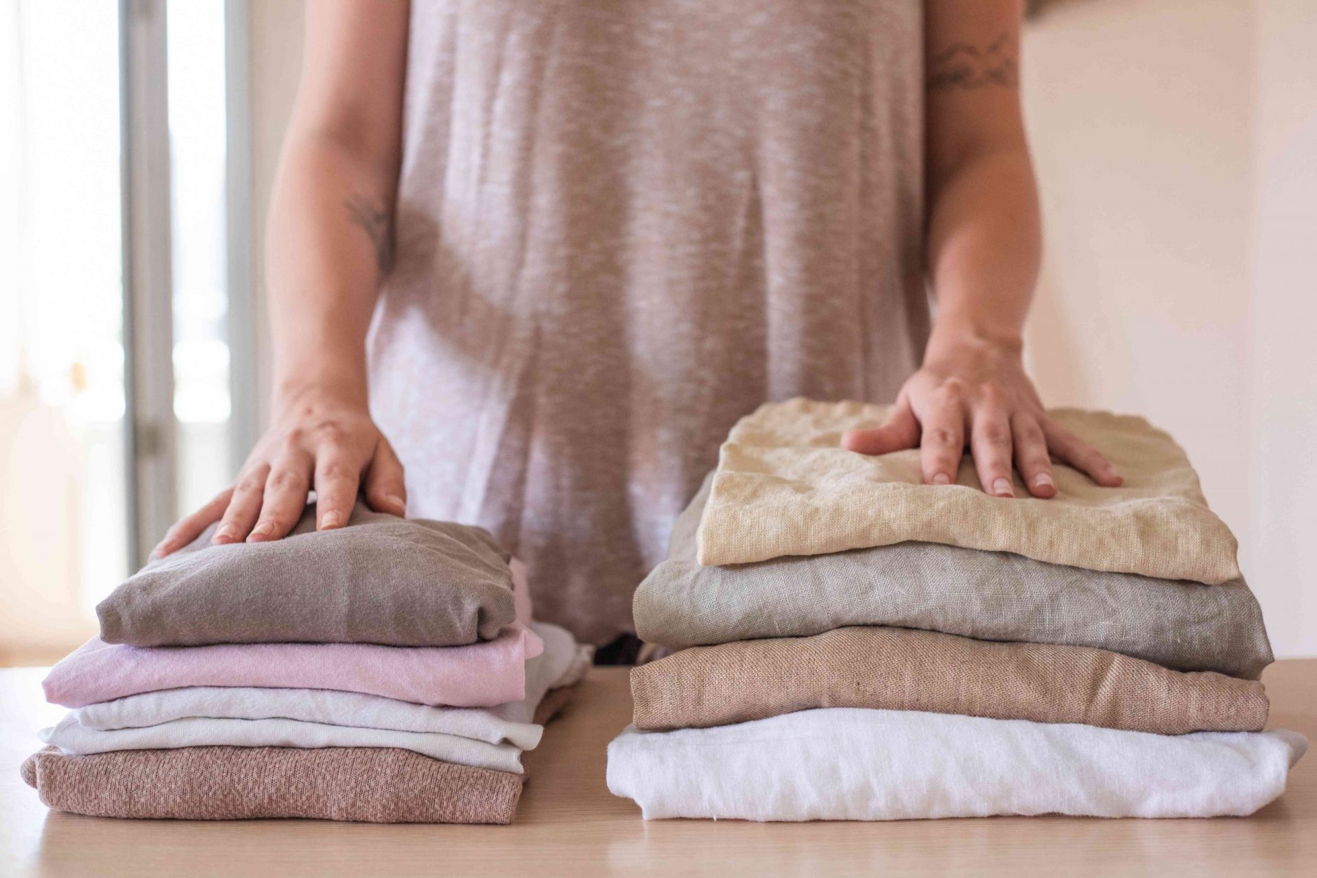 una persona delante de dos pilas de ropa dobladas: una de algodón y otra de lino