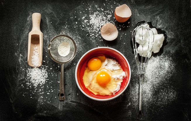 Un bol con huevos, algo de harina y un batidor sobre una mesa negra