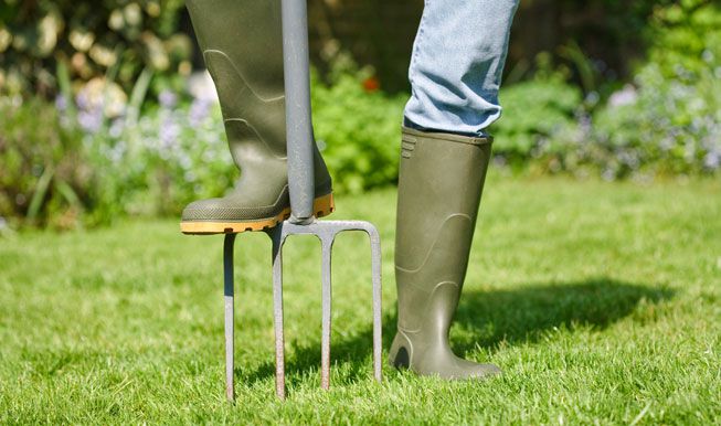 Una persona con botas de jardinero airea el césped