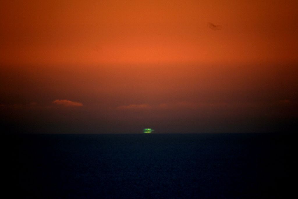 Destello verde de luz en el horizonte rodeado de un cielo naranja brillante al atardecer