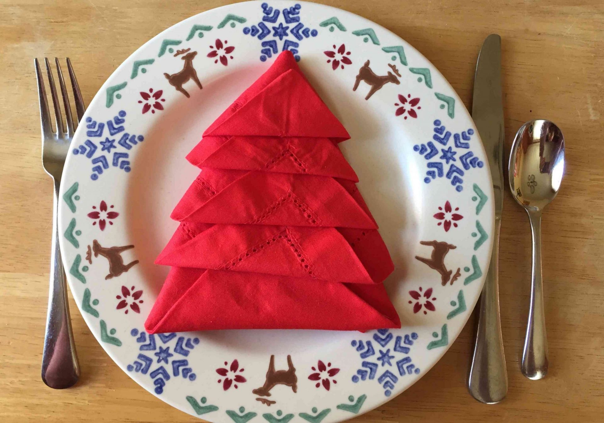 servilleta roja doblada en forma de árbol de Navidad sobre plato de renos