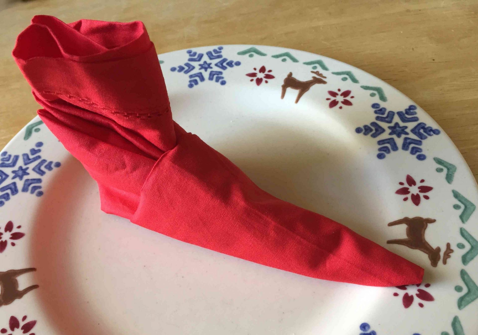 servilleta roja doblada en forma de bota de elfo sobre plato de reno