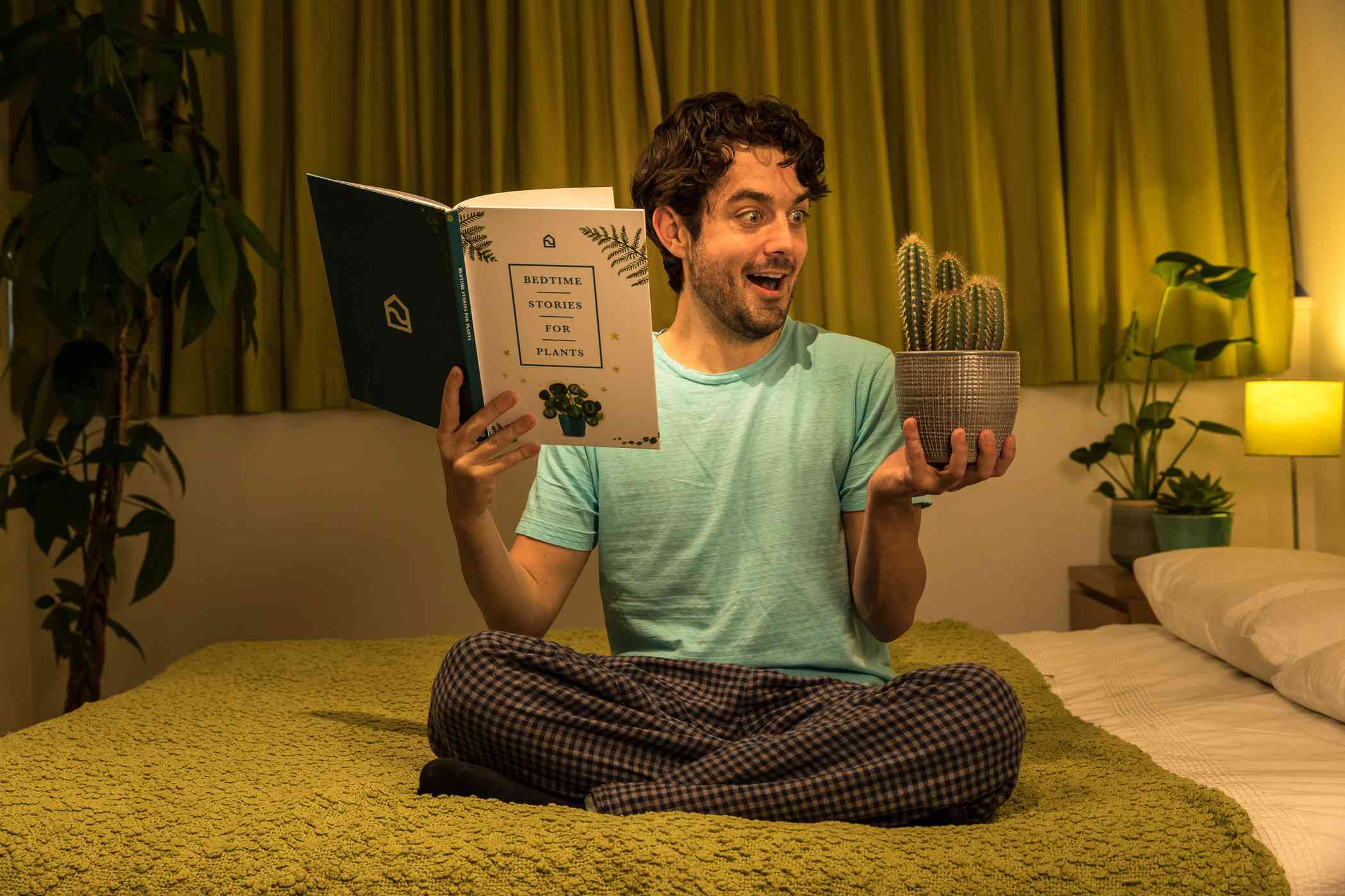 un hombre sostiene un libro y una planta en sus manos mientras está en la cama