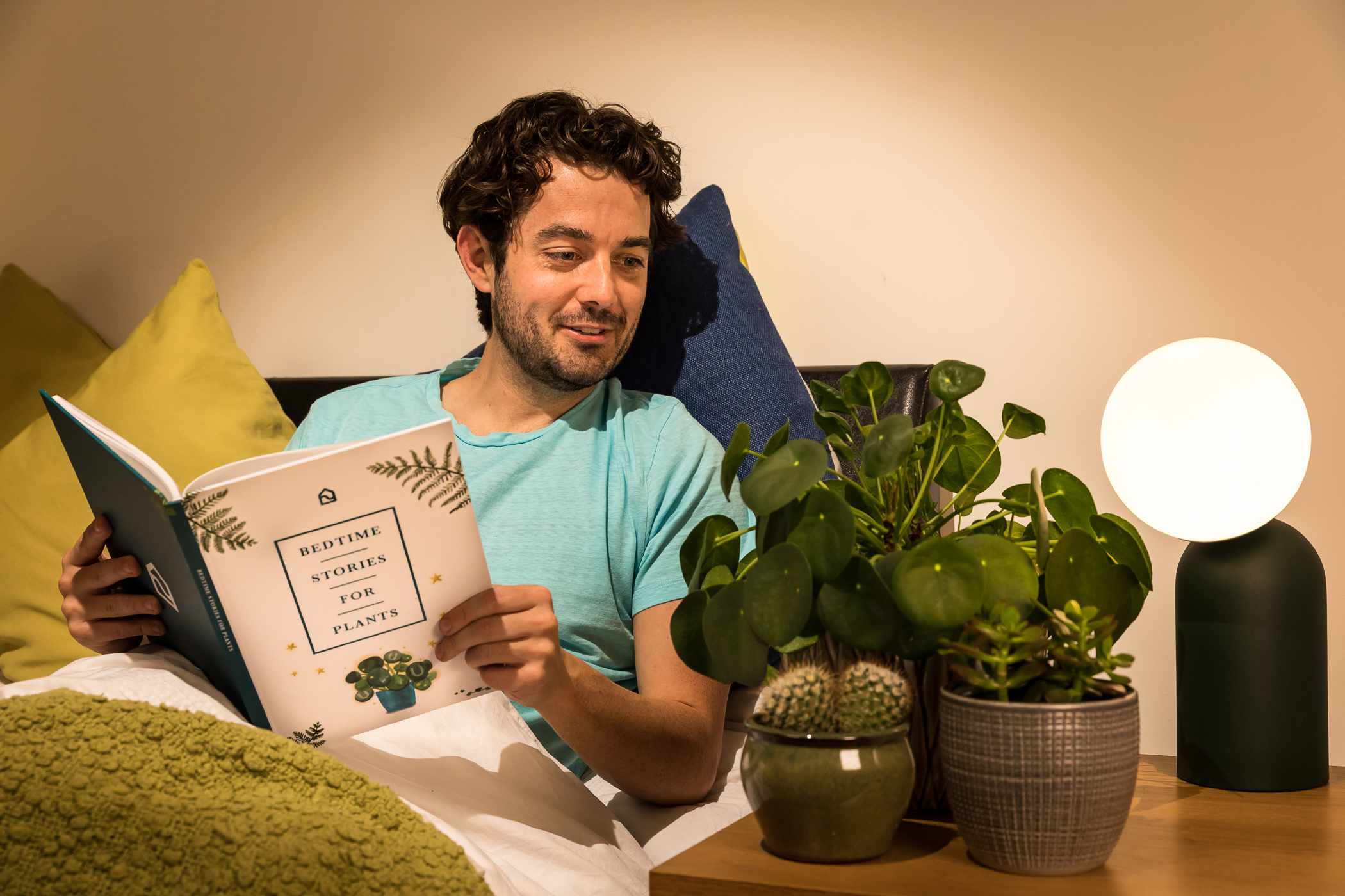 un tipo en la cama lee un libro a sus tres plantas