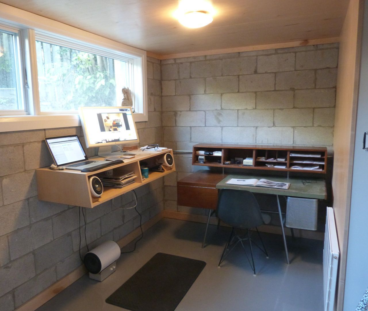 Un montaje de oficina con un escritorio y almacenamiento en una pequeña habitación con paredes de bloques de hormigón