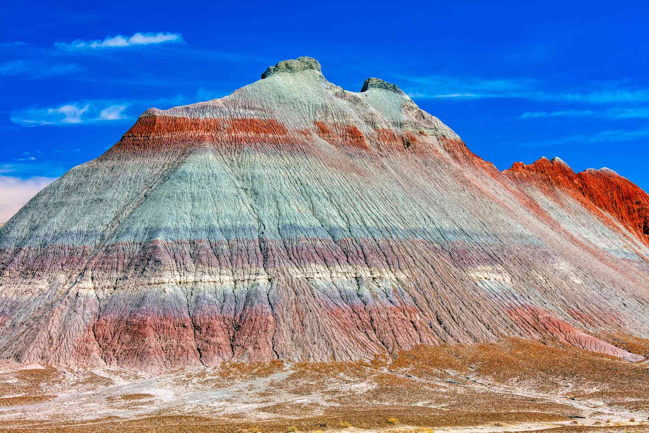 Una montaña en el desierto con capas de piedra roja, gris, azul y morada