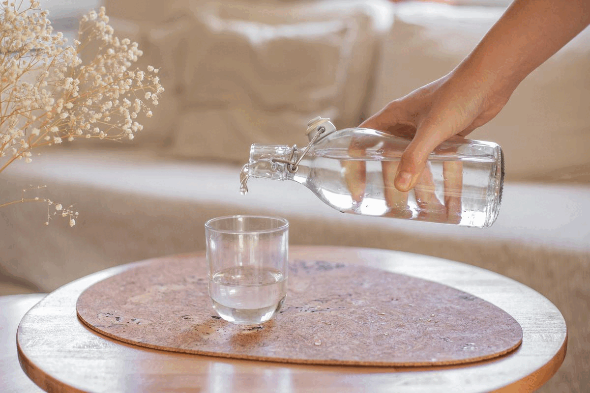 una mano vierte agua de una jarra de cristal en un vaso de cristal sobre una mesa de madera