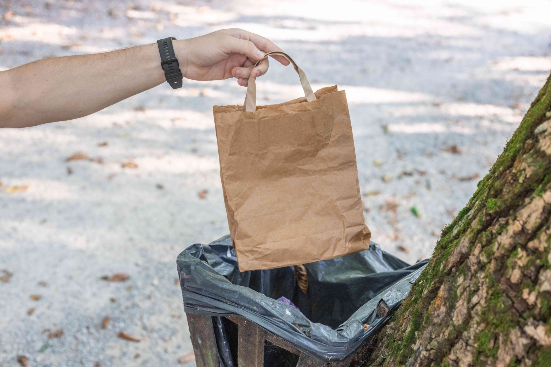 un excursionista tira una bolsa de papel marrón en la papelera del camping