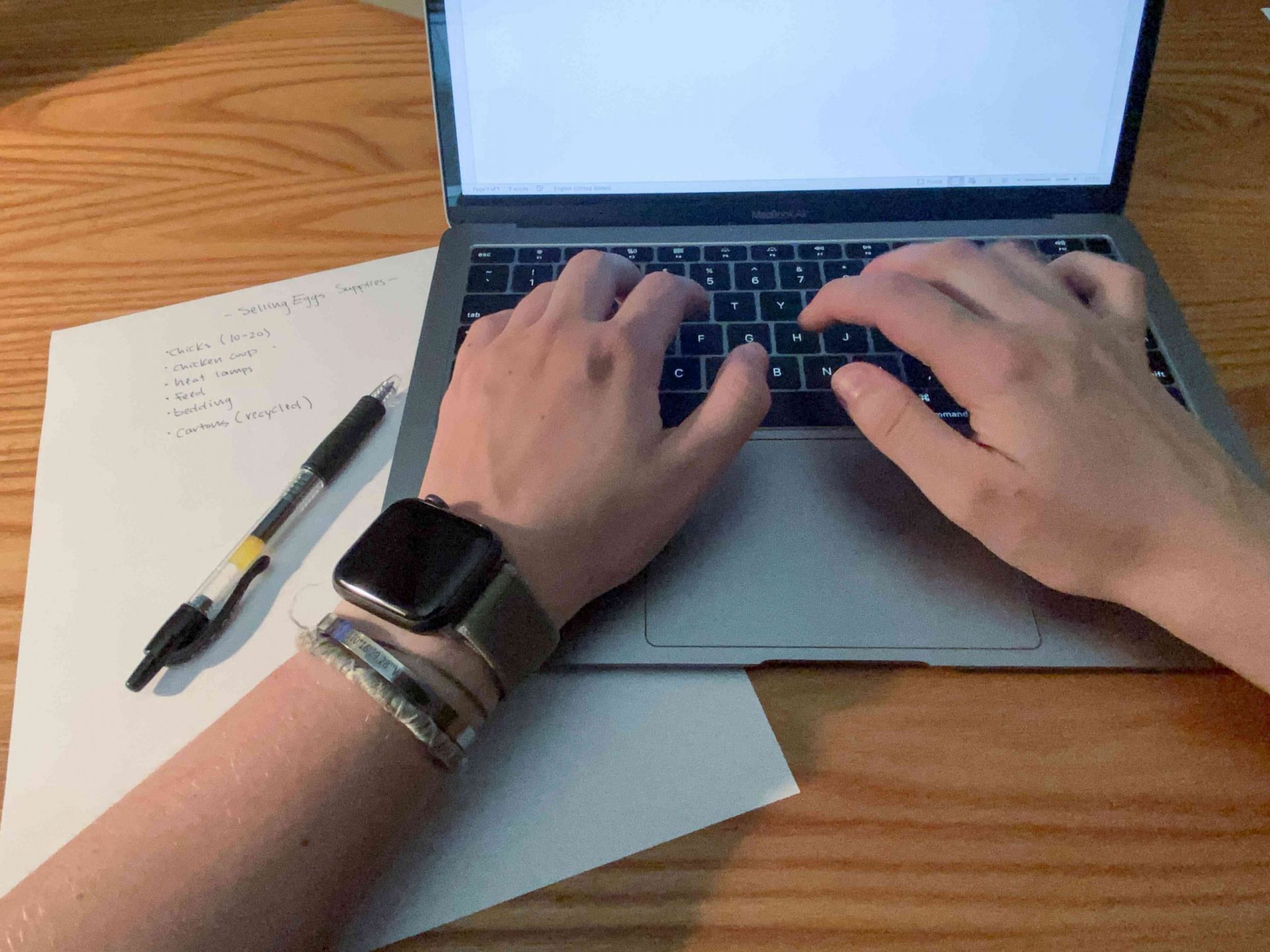 una persona con un apple watch trabaja en un portátil con notas escribiendo un plan de negocio
