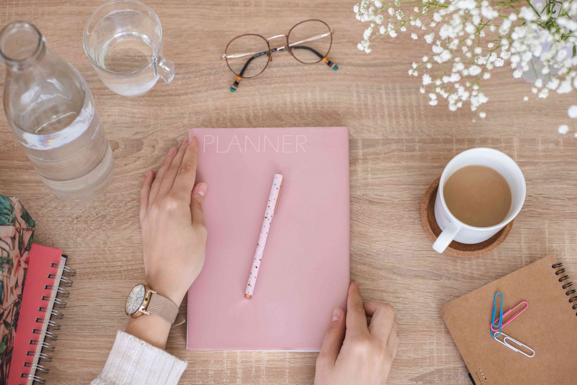 plano de las manos de una persona tocando una agenda rosa pálido sobre un escritorio de madera