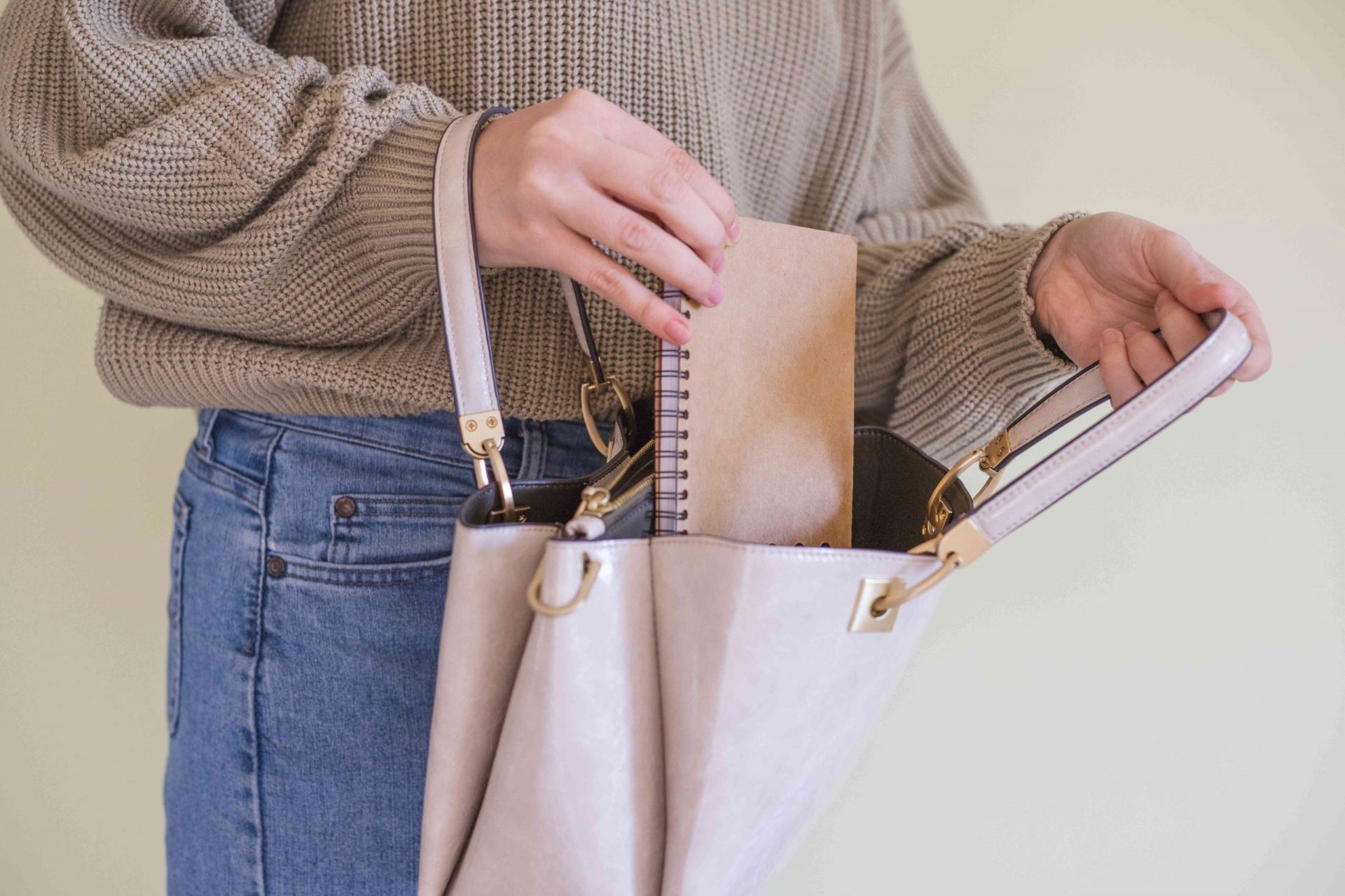 una persona con jersey deja caer una pequeña agenda de papel en un bolso de cuero marrón claro