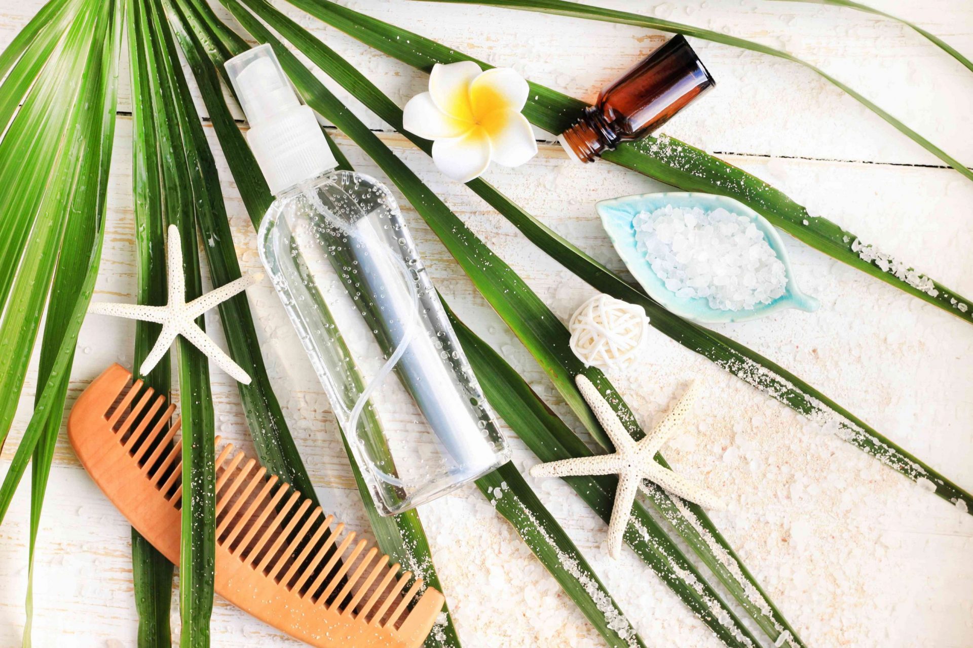 Kit de belleza de verano. Botella de spray mineral de sal marina para el cabello y el cuerpo vista desde arriba sobre una hoja de palmera verde