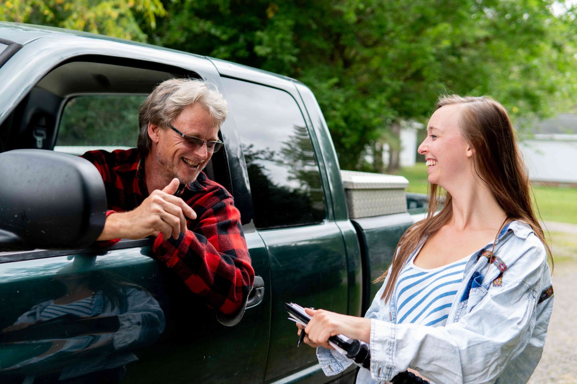 un hombre mayor en un camión se asoma a la ventana para hablar con una joven con un portapapeles
