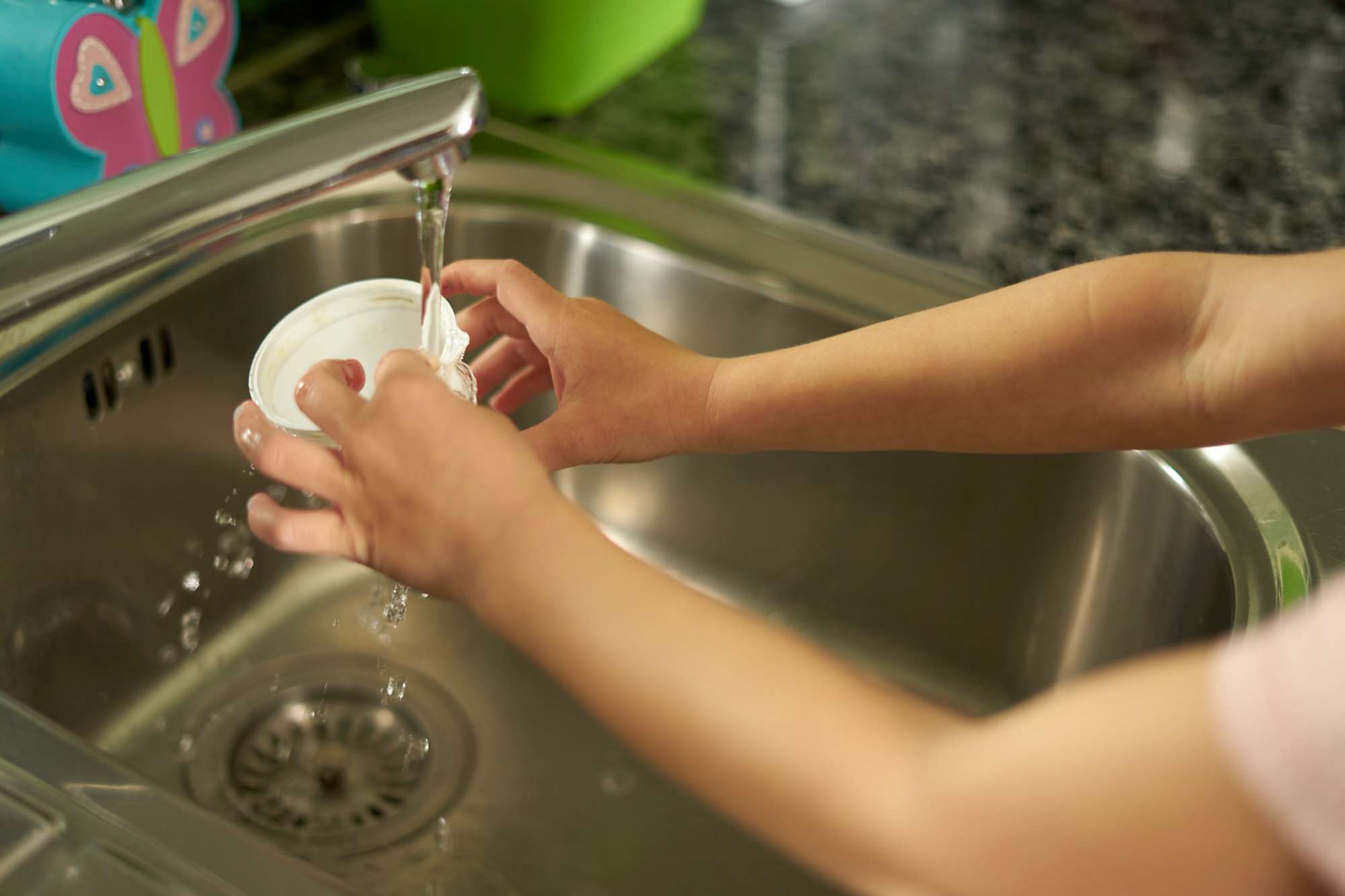 las manos del niño aclaran el vaso de plástico en el fregadero de la cocina antes de reciclarlo