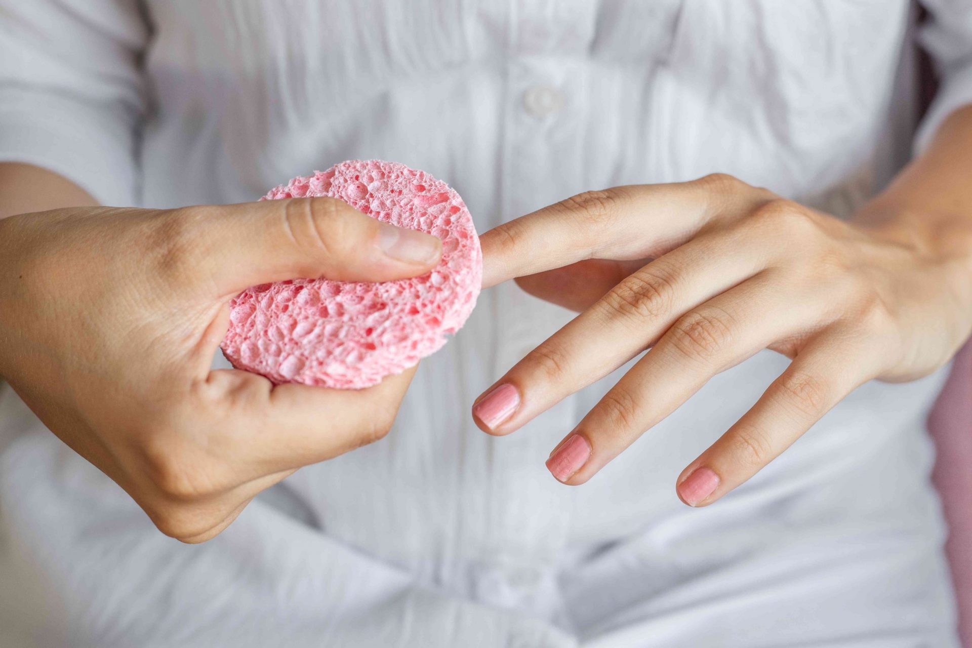 mujer con blusa blanca utiliza una esponja rosa para quitarse el esmalte de uñas