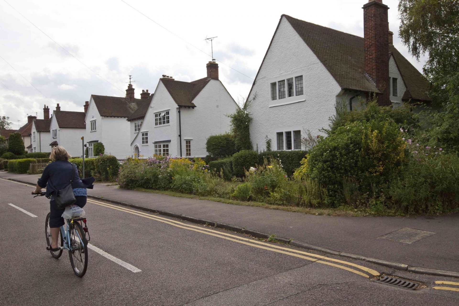 Reino Unido - Letchworth Garden City - Una mujer pasa con su bicicleta por delante de las casas de época Arts and Crafts