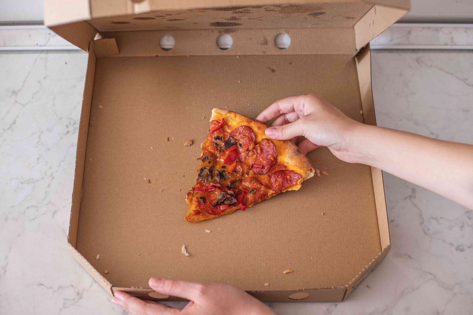 manos buscan la última porción de pizza en una caja de cartón abierta
