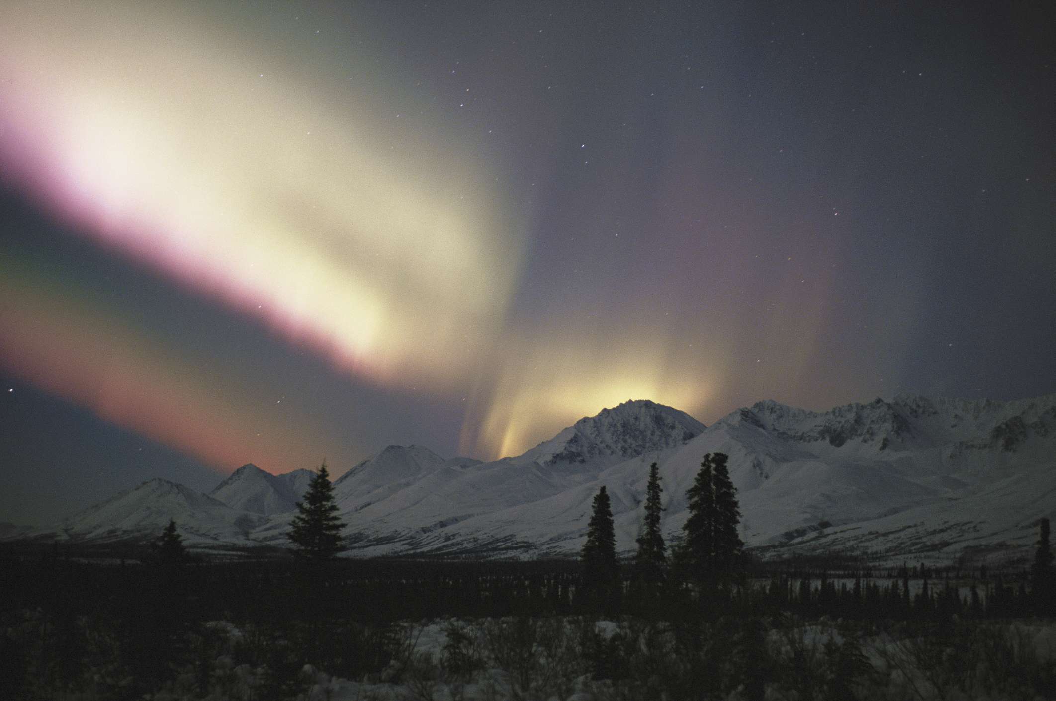 Aurora boreal blanca y rosa sobre montañas nevadas