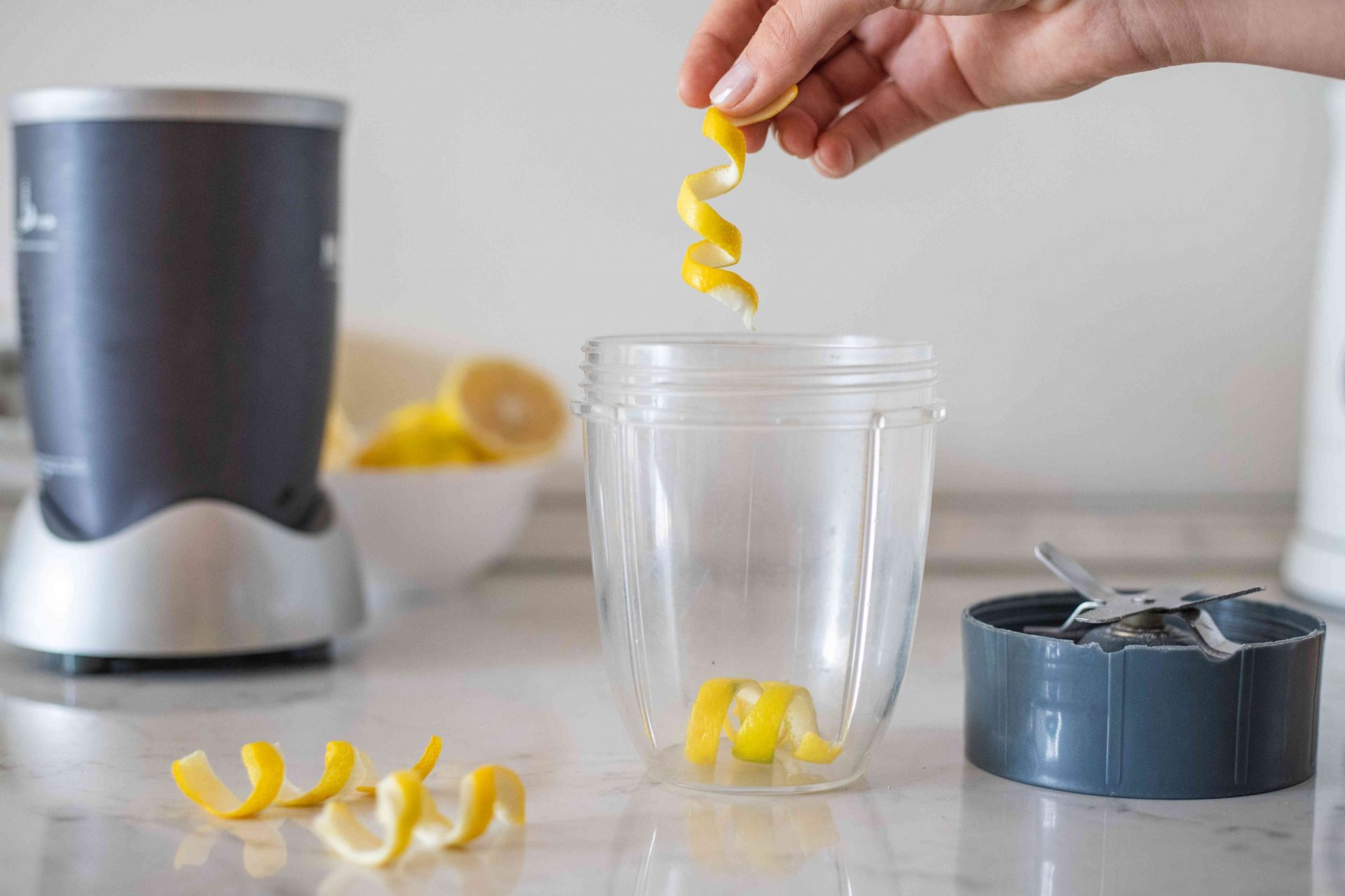 la mano deja caer la cáscara de limón en una batidora pequeña para pulverizarla y convertirla en cáscara de cítricos