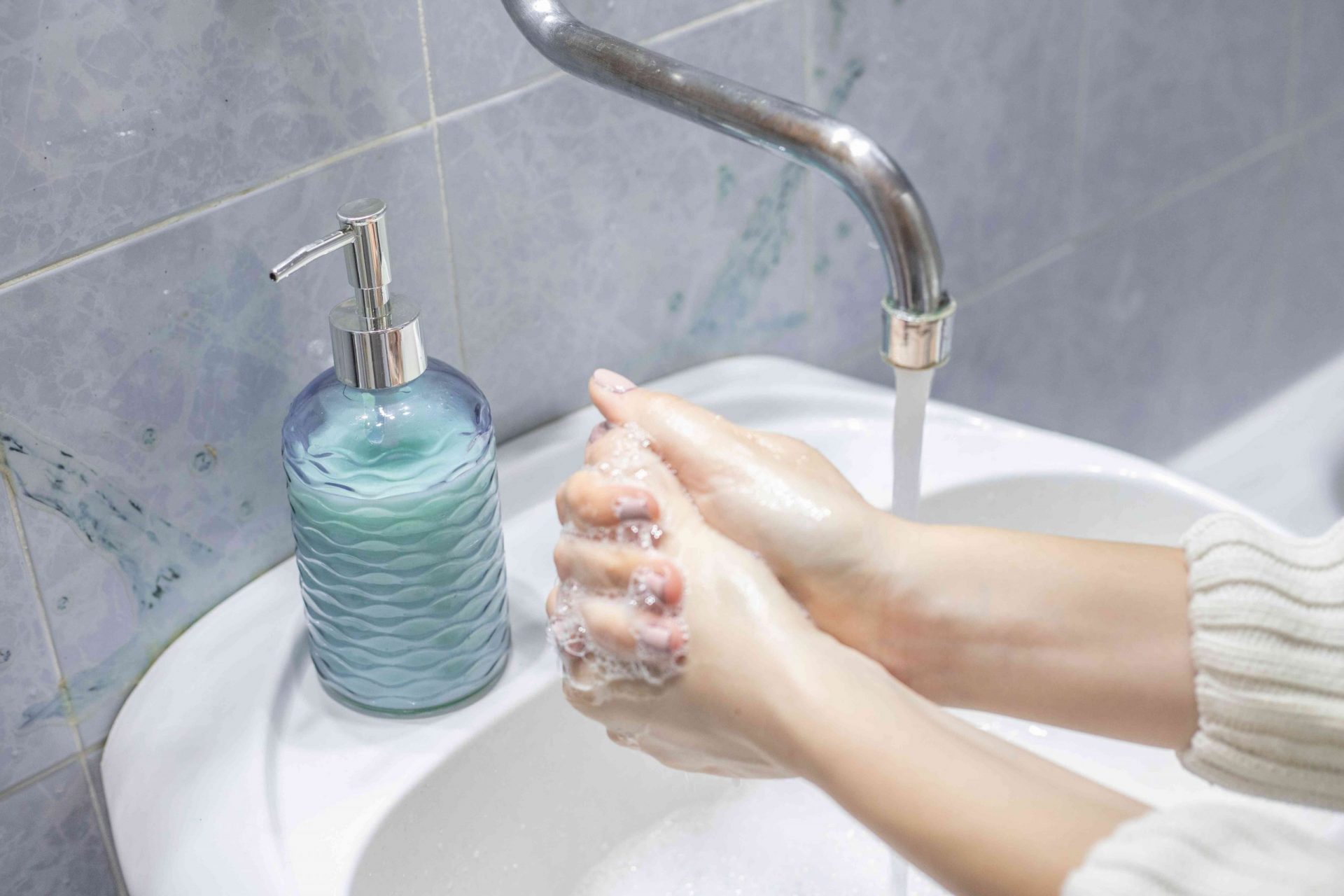 una persona con jersey se lava las manos con una botella de cristal rellenable en el lavabo