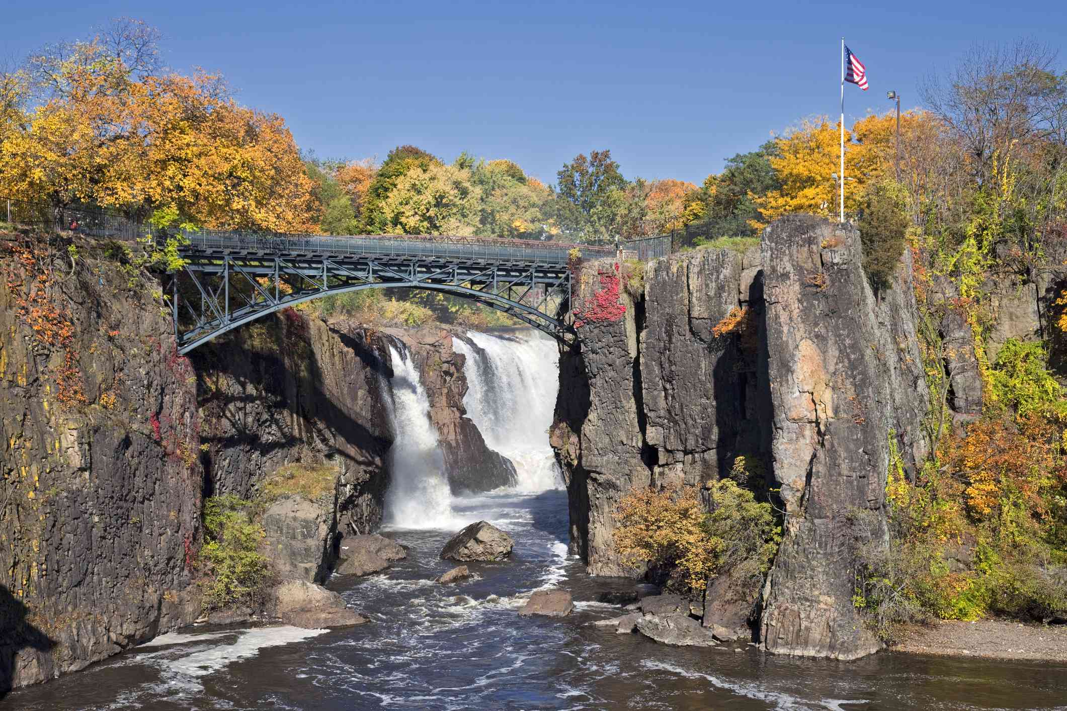 cascada detrás del puente, rodeada de altas rocas y árboles de colores durante el otoño
